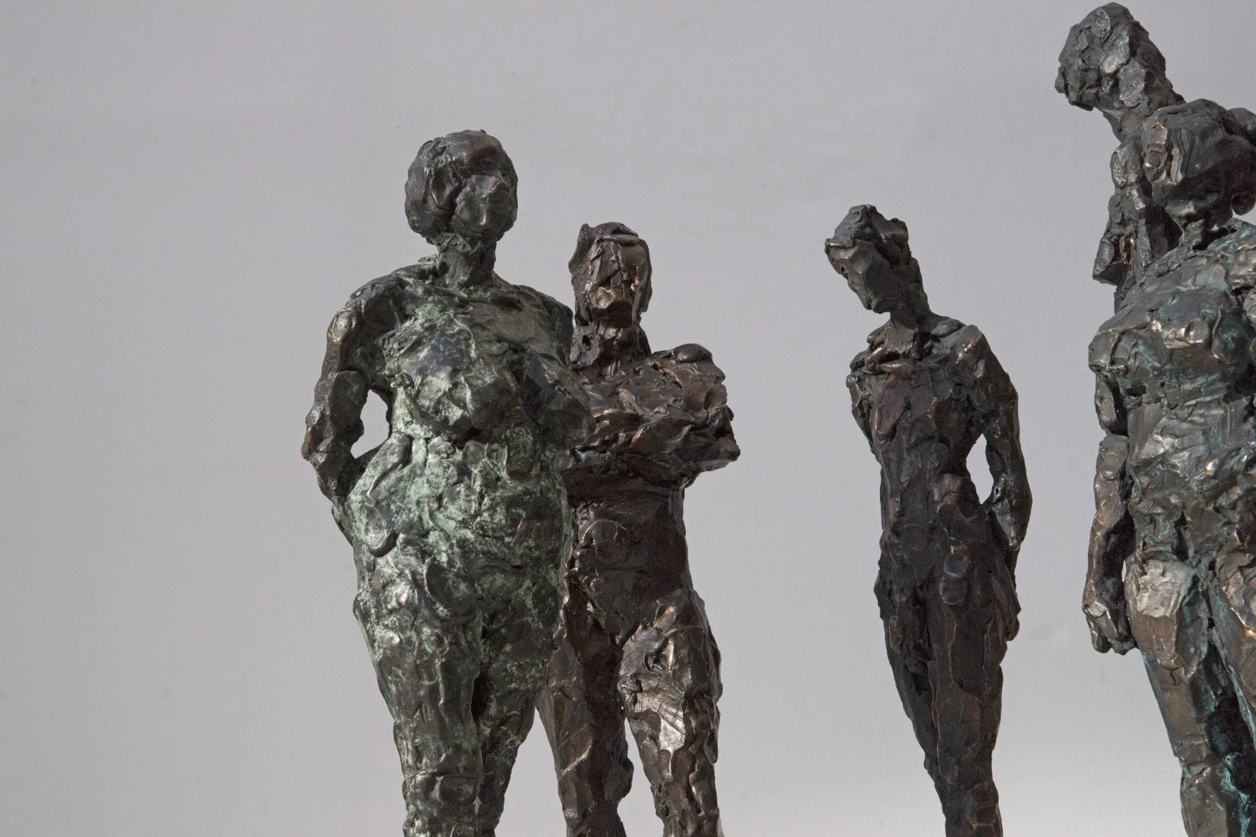 Vier abstrakte Bronzeskulpturen von Frauen, die in einer Gruppe stehen, vor einem neutralen grauen Hintergrund.

