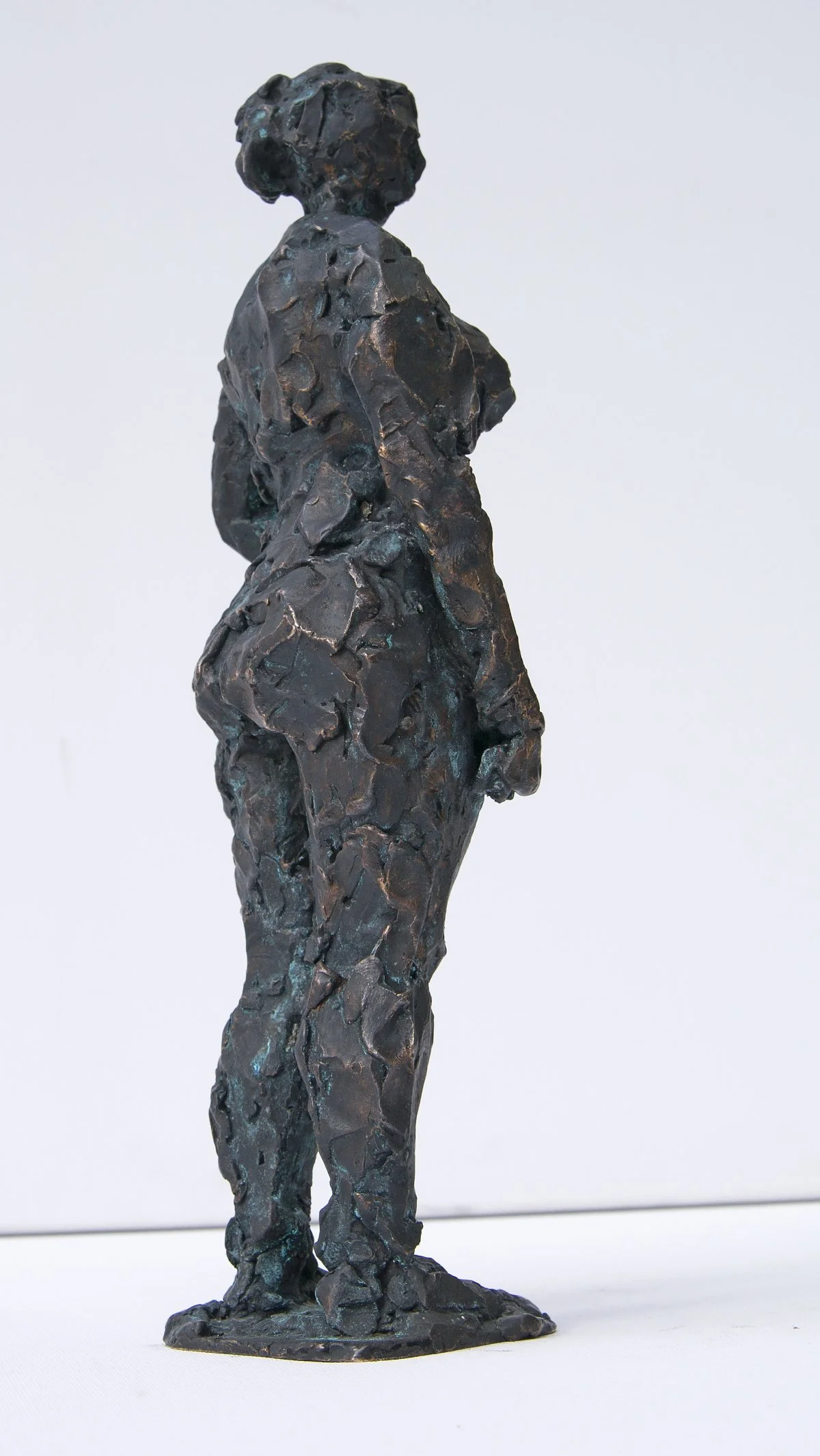 Eine schwarze, strukturierte Skulptur einer stehenden Frau mit kurzem Haar, die zur Seite blickt, vor einem schlichten hellen Hintergrund.
