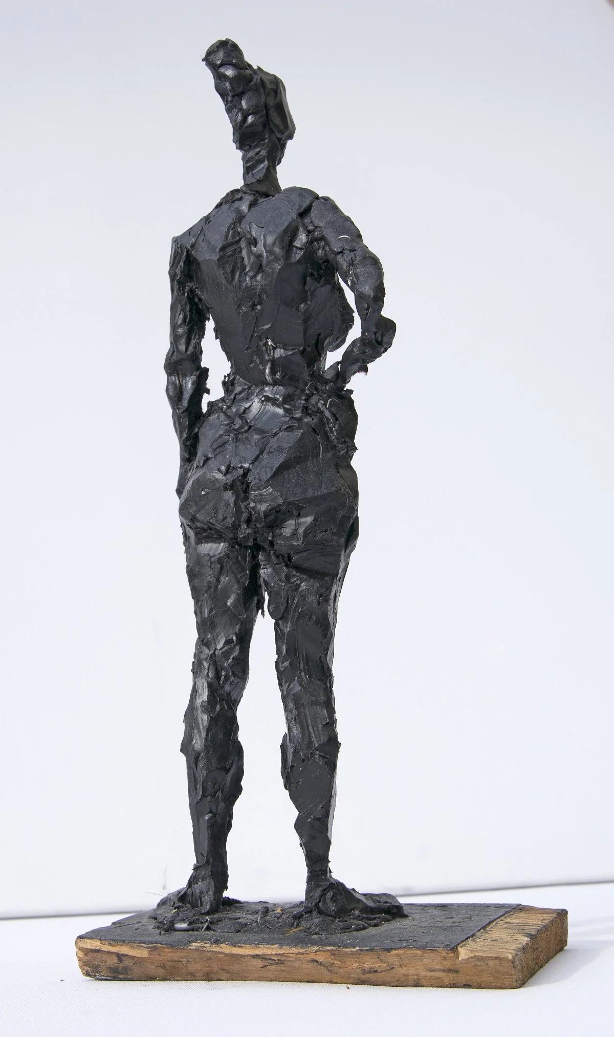 Skulptur einer Frau, die mit der Hand in der Hüfte steht, aus dunklem, strukturiertem Material, montiert auf einem Holzsockel.

