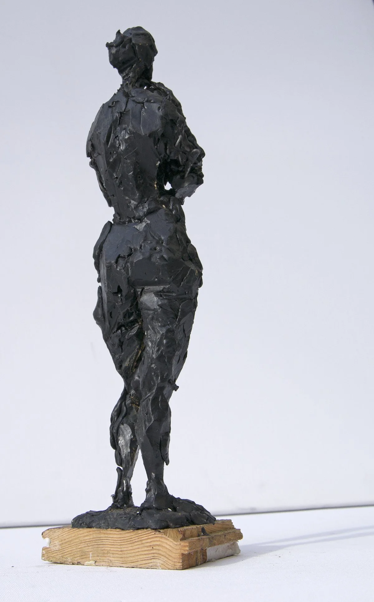 Eine kleine Skulptur einer stehenden Person aus dem dunklen, glänzenden Material, montiert auf einem Holzsockel.
