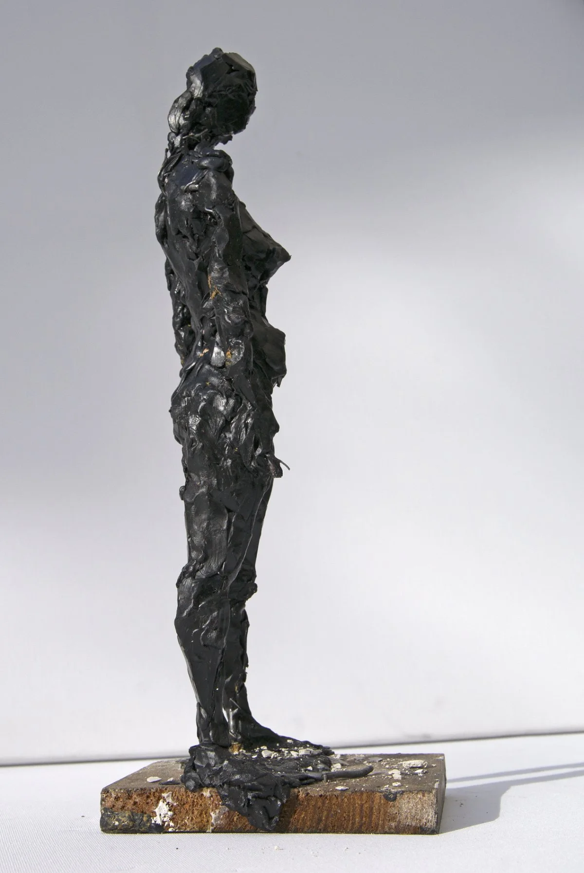 Eine schwarze, strukturierte Skulptur einer stehenden Frau auf einem rechteckigen Sockel.
