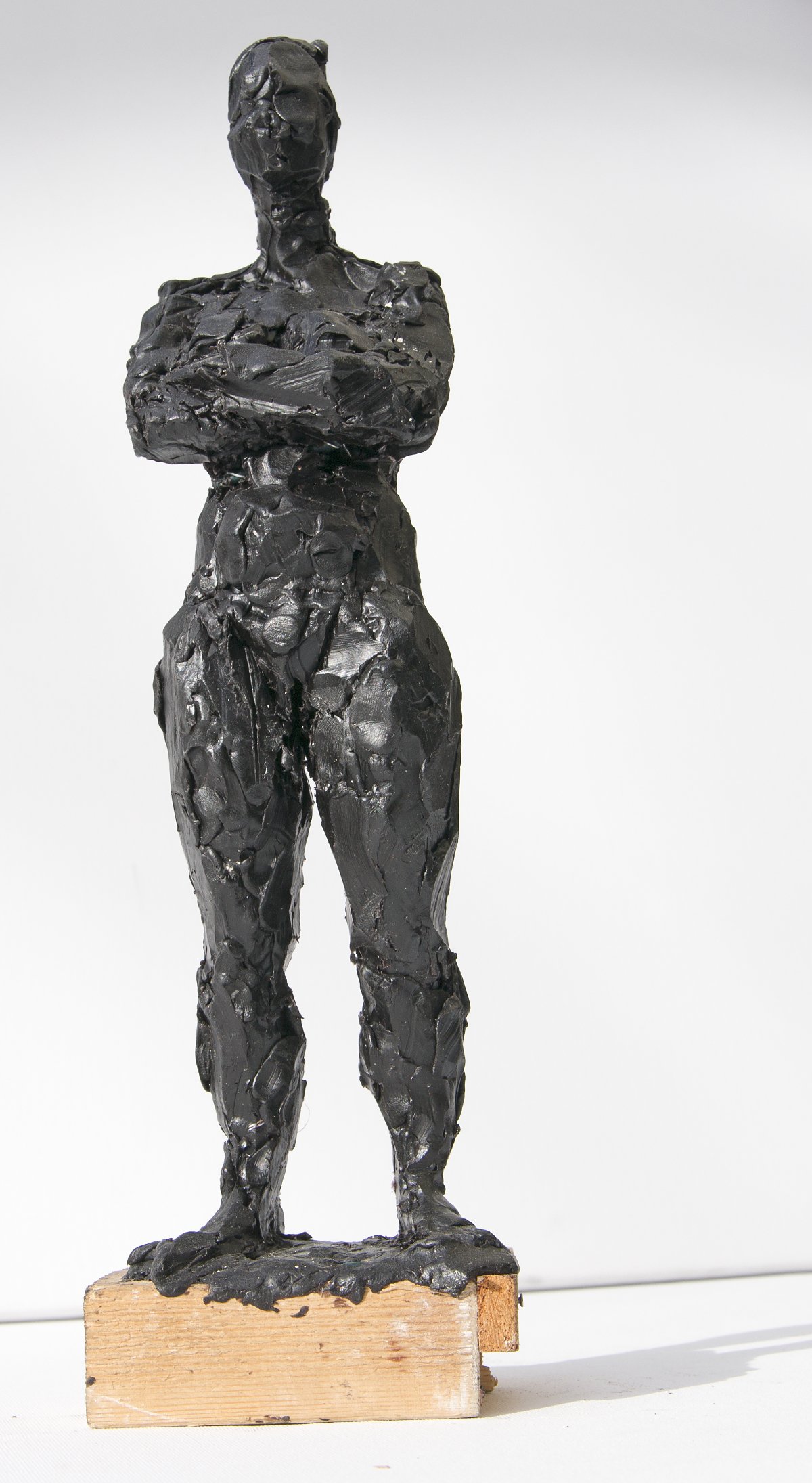 Schwarze abstrakte Skulptur einer stehenden Frau mit verschränkten Armen auf einem Holzsockel.
