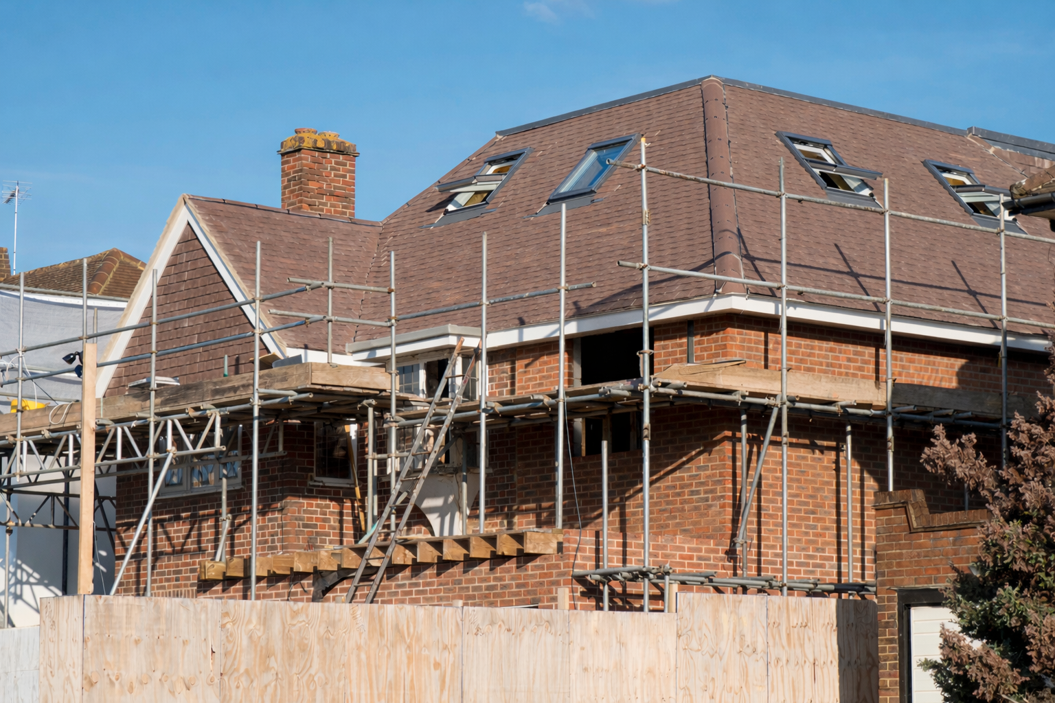 A house under renovation with scaffolding around it, showing a brick exterior and a roof with multiple skylights.