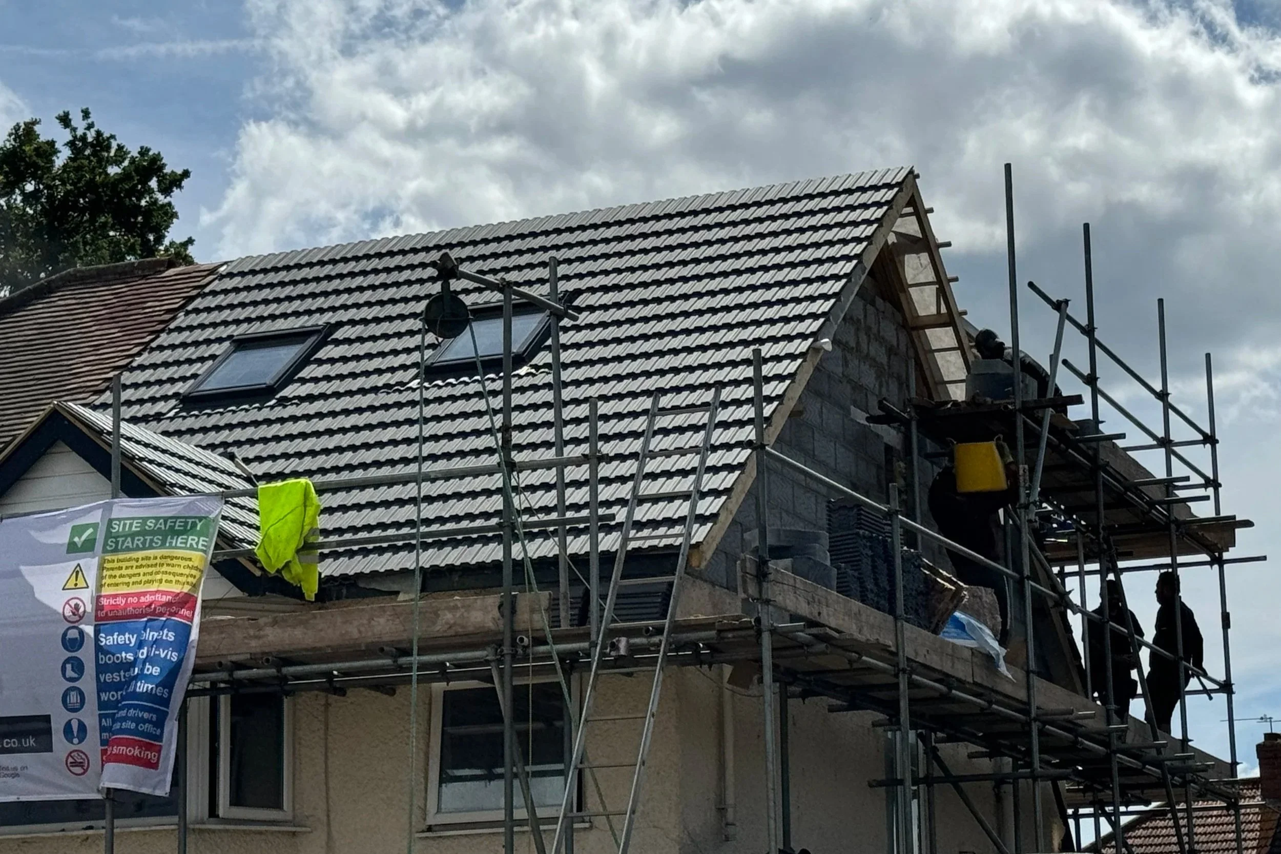 Construction workers on scaffolding installing or repairing roof shingles on a residential house during daytime.