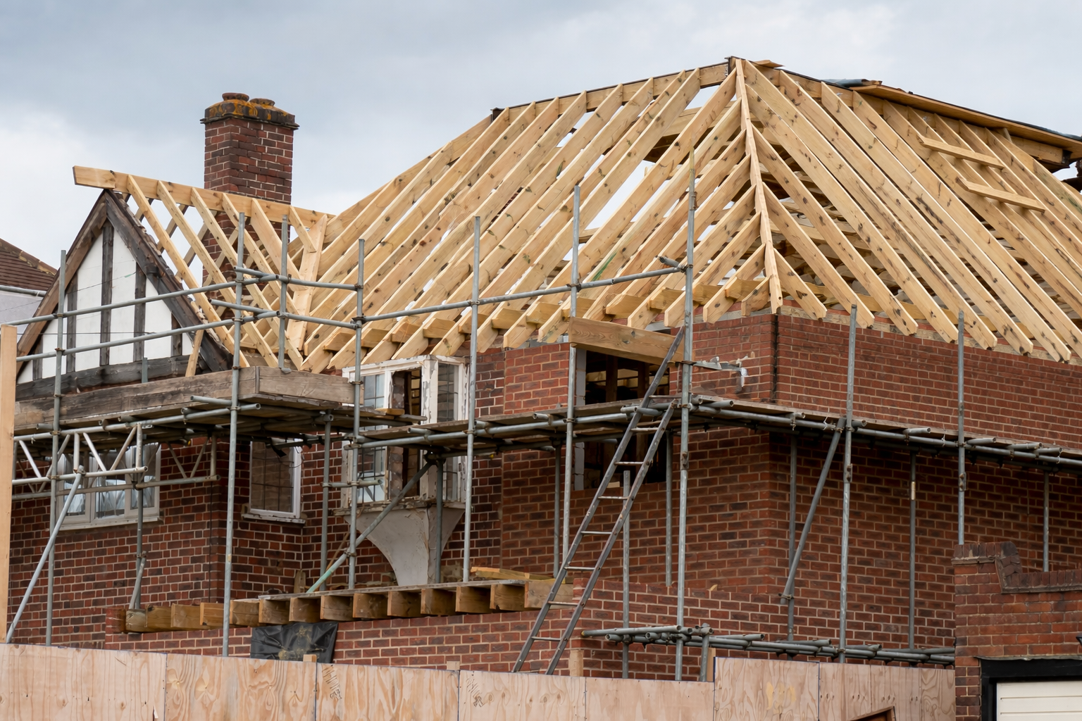 House under construction with scaffolding and new roof framing in progress.