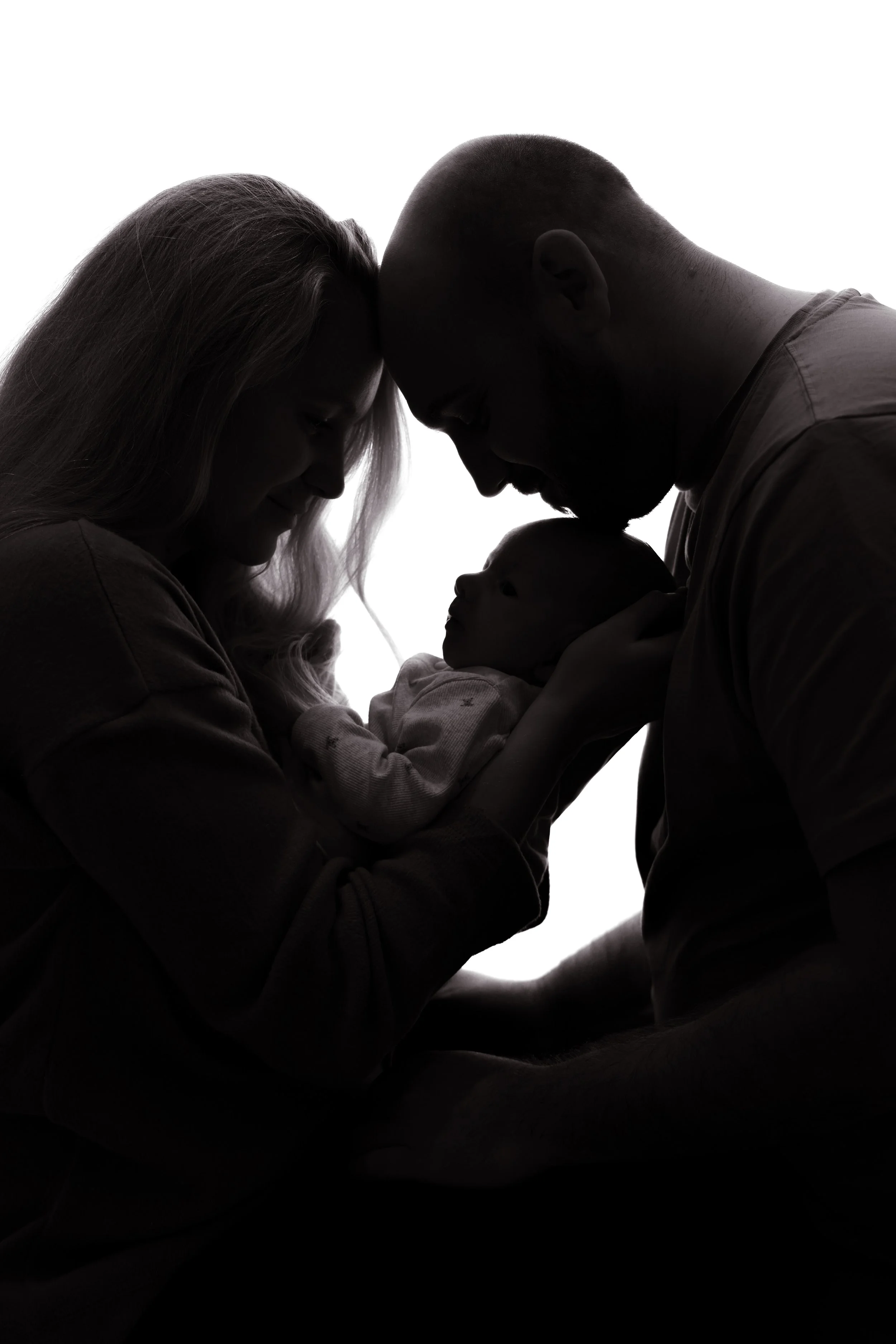Silhouette of a family – mother, father, and baby – with faces touching, creating a tender and intimate scene.