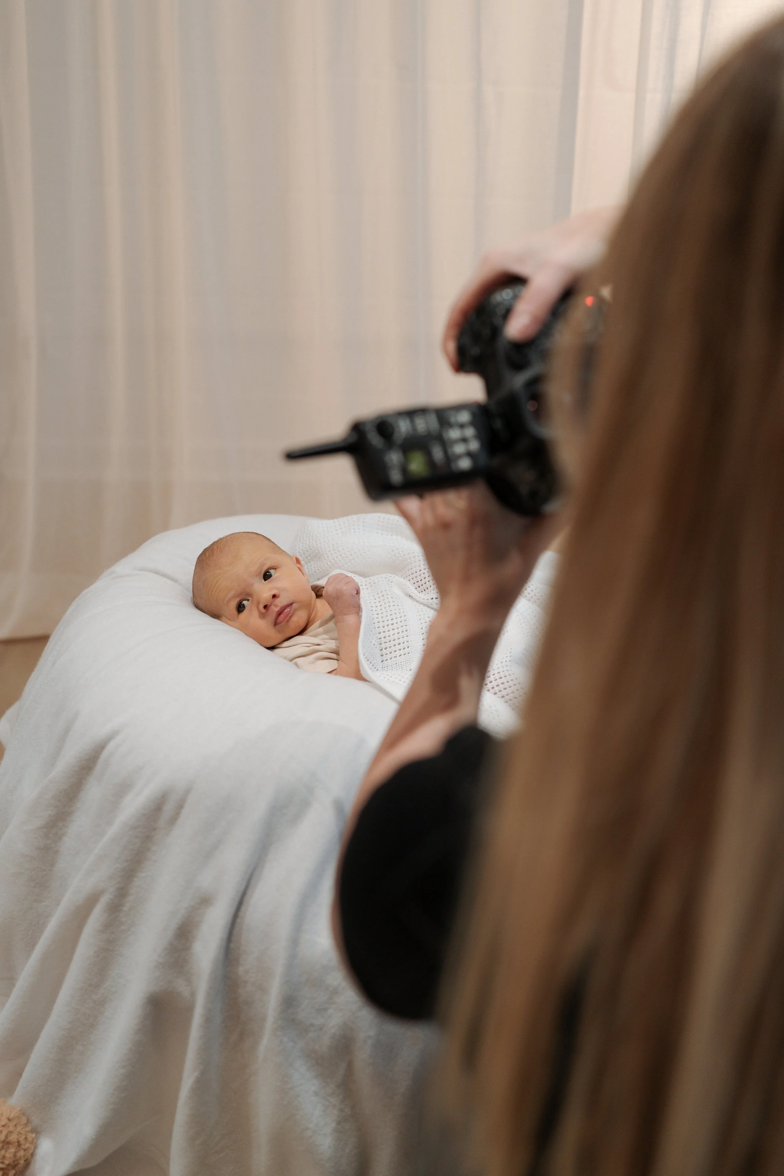 A woman taking a photo of a baby lying on a bed with a camera