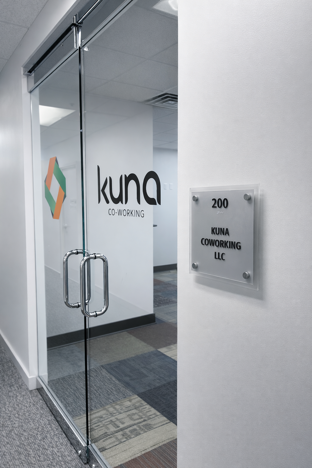 Office entrance with glass door displaying 'Kuna Co-Working' logo and a wall plaque showing the address '200 Kuna Coworking LLC'.