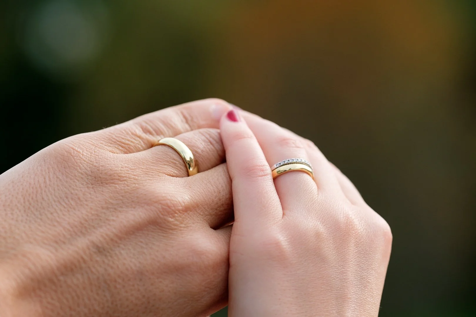 Nahaufnahme zweier Hände, die jeweils einen Ehering tragen, während sie sich berühren. Hintergrund unscharf.