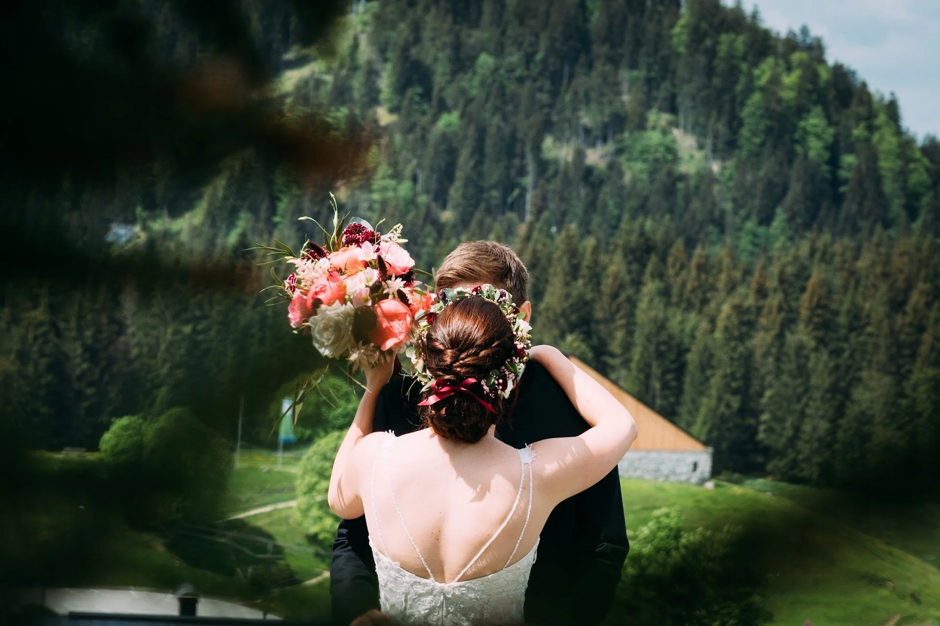 Ein Brautpaar in der Natur, die Braut umarmt den Bräutigam, mit Blick auf einen bewaldeten Hügel im Hintergrund.