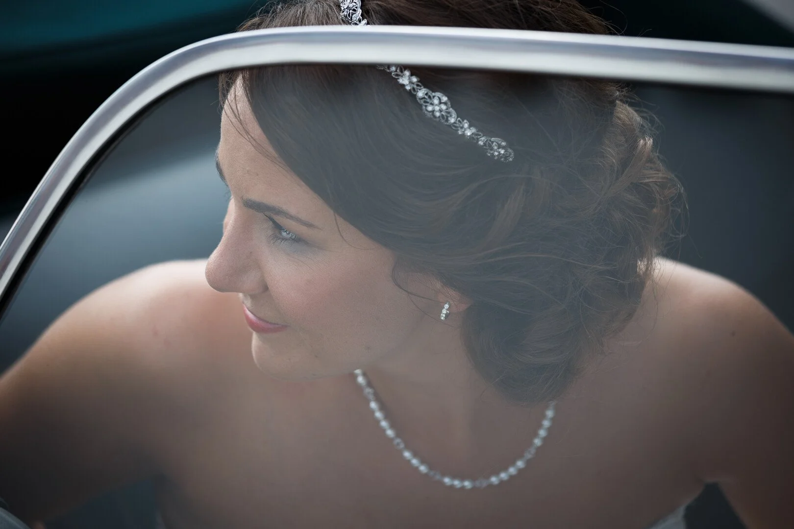 Eine Frau in einem weißen Brautkleid mit Perlenkette und Haarschmuck, sitzt im Auto.