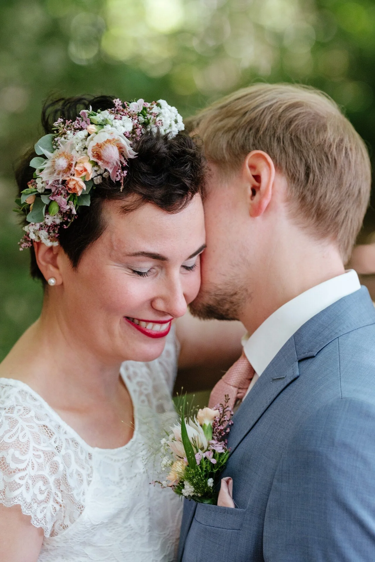 Ein Brautpaar bei einer Hochzeit, innig zusammen, trinkt, umarmt sich, in einer grünen, natürlichen Umgebung, mit Blumen und Bäumen im Hintergrund
