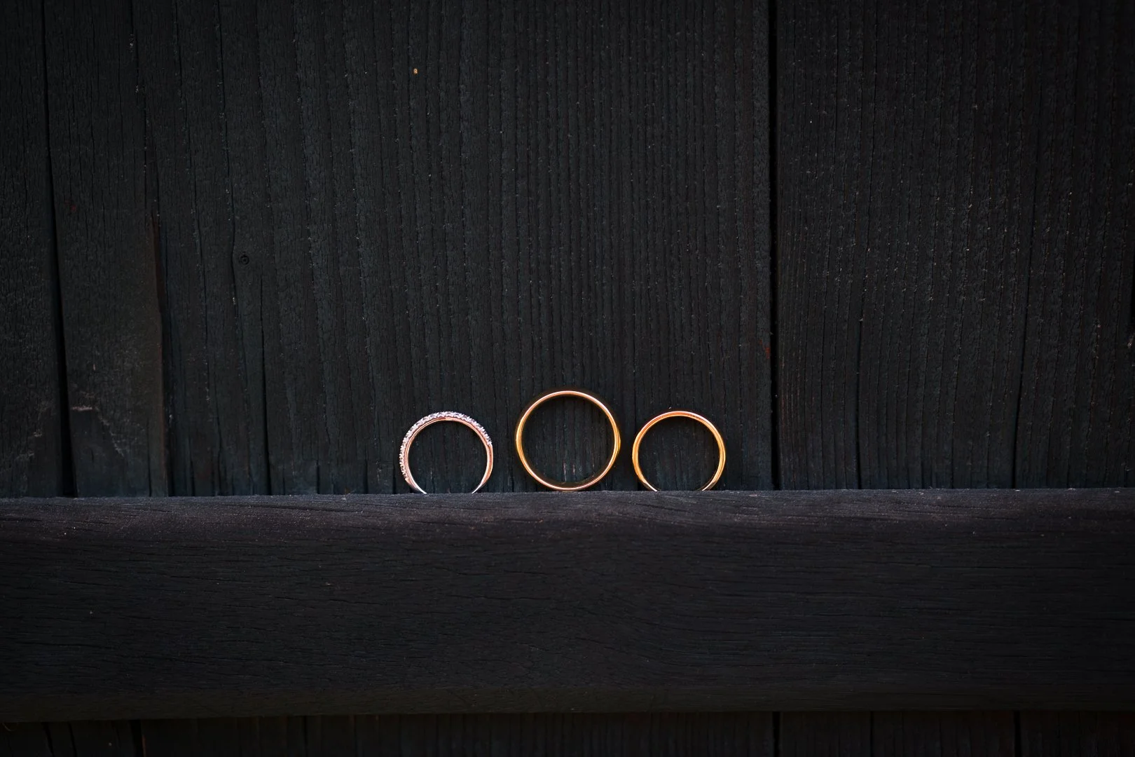 Drei goldene Ringe auf einem schwarzen Holzregal vor einer schwarzen Holzwand.