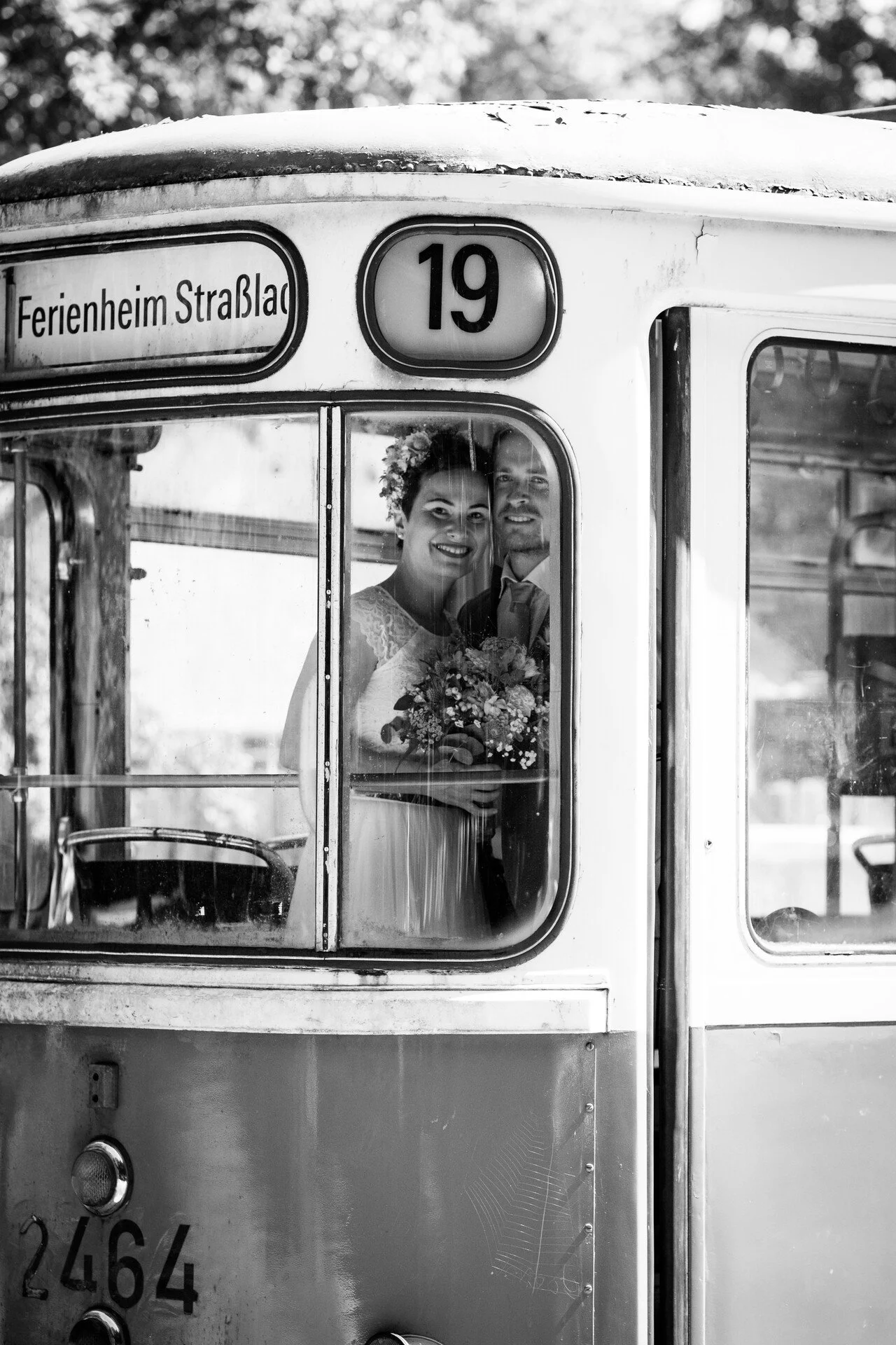 Ein Brautpaar schaut beim Shooting durch eine Münchner Trambahn, die Braut hält einen Blumenstrauß. Das Bild ist schwarz-weiß.