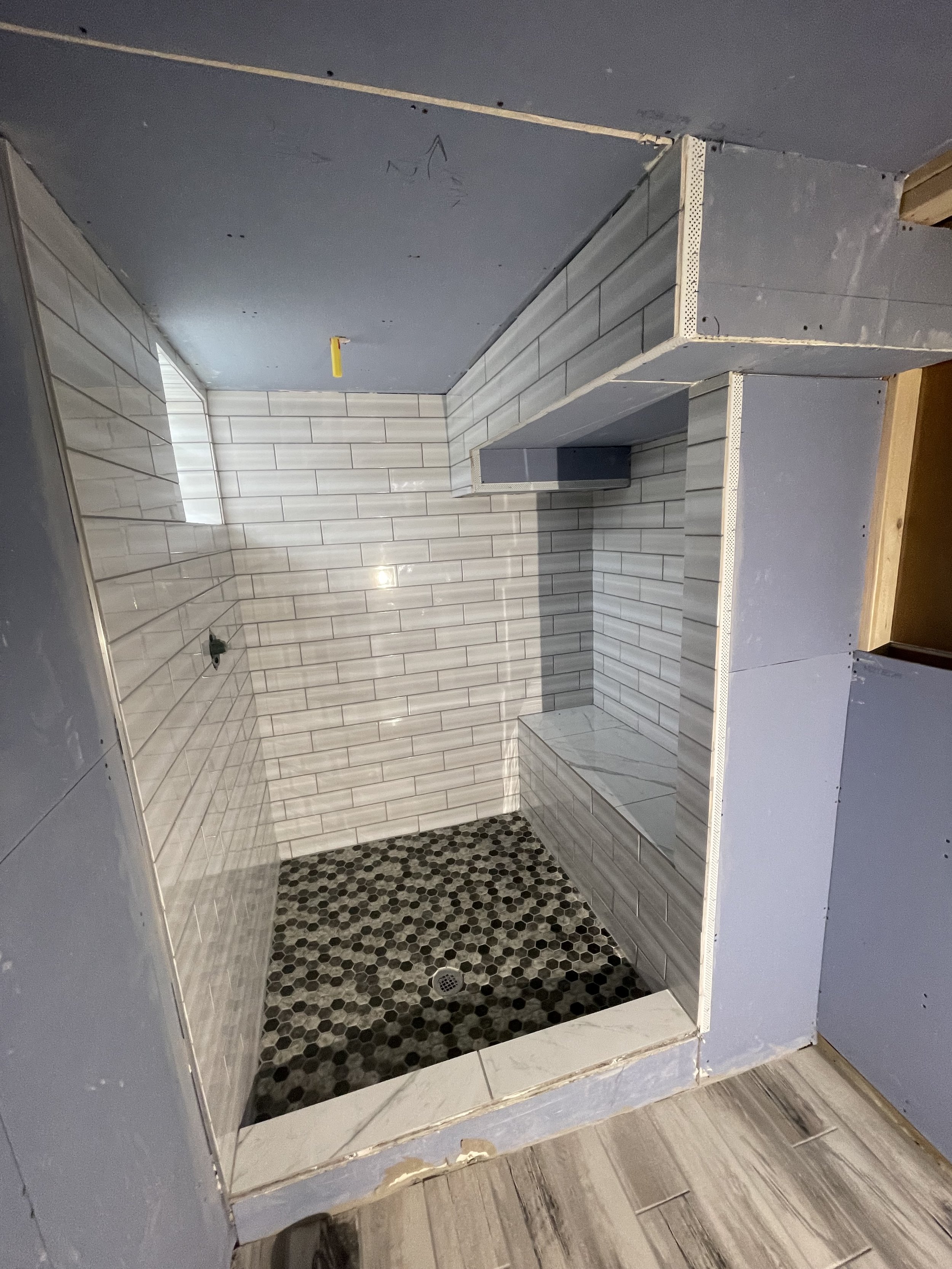 A shower stall under construction, with tiled walls, a built-in bench, and a mosaic tile floor, surrounded by unfinished wall panels.


Installed near Hamilton Ohio 