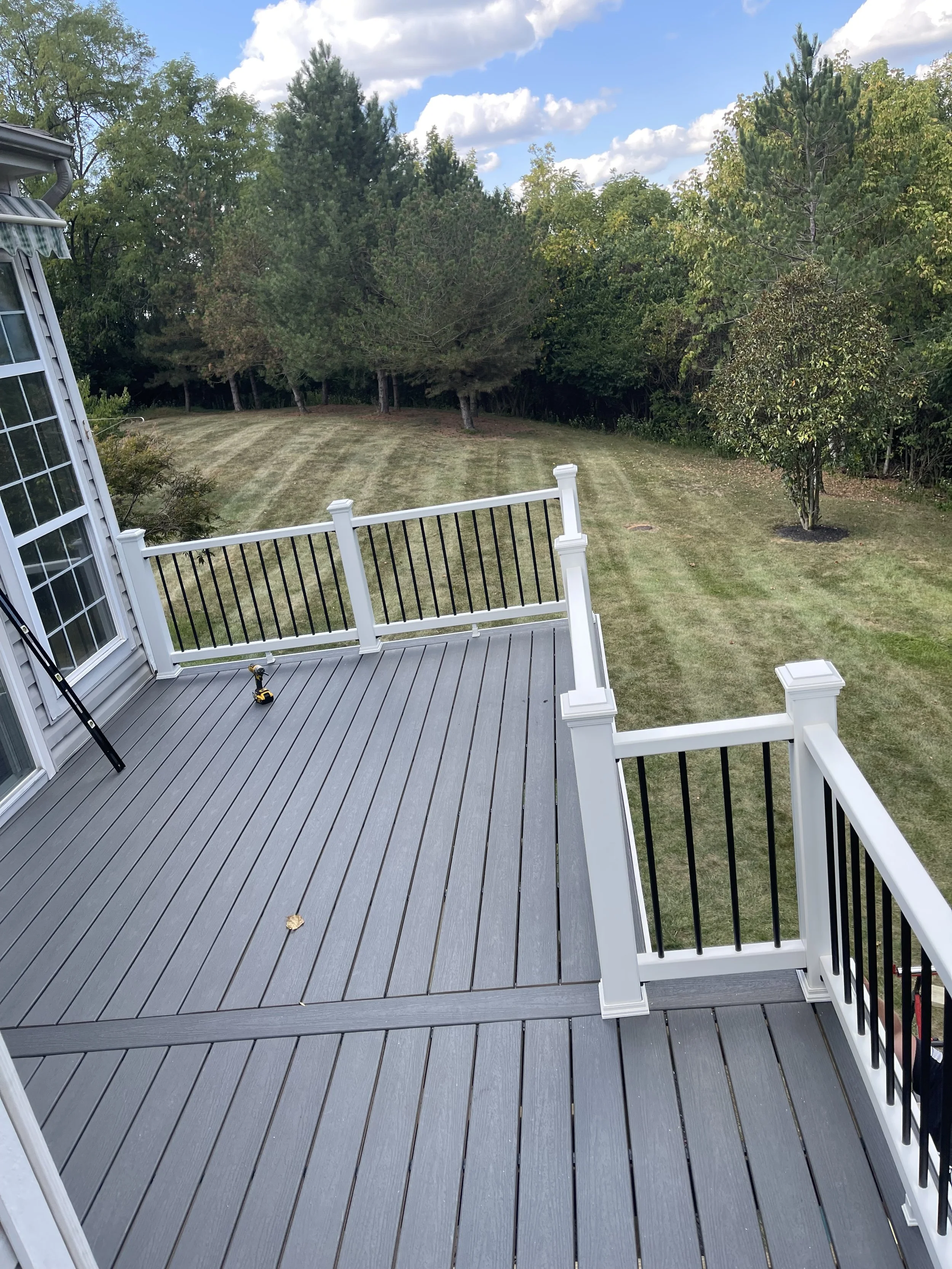 View of a new gray deck with black and white railing overlooking a backyard with a grassy lawn, trees, and a partly cloudy sky.


Installed near Cincinnati Ohio