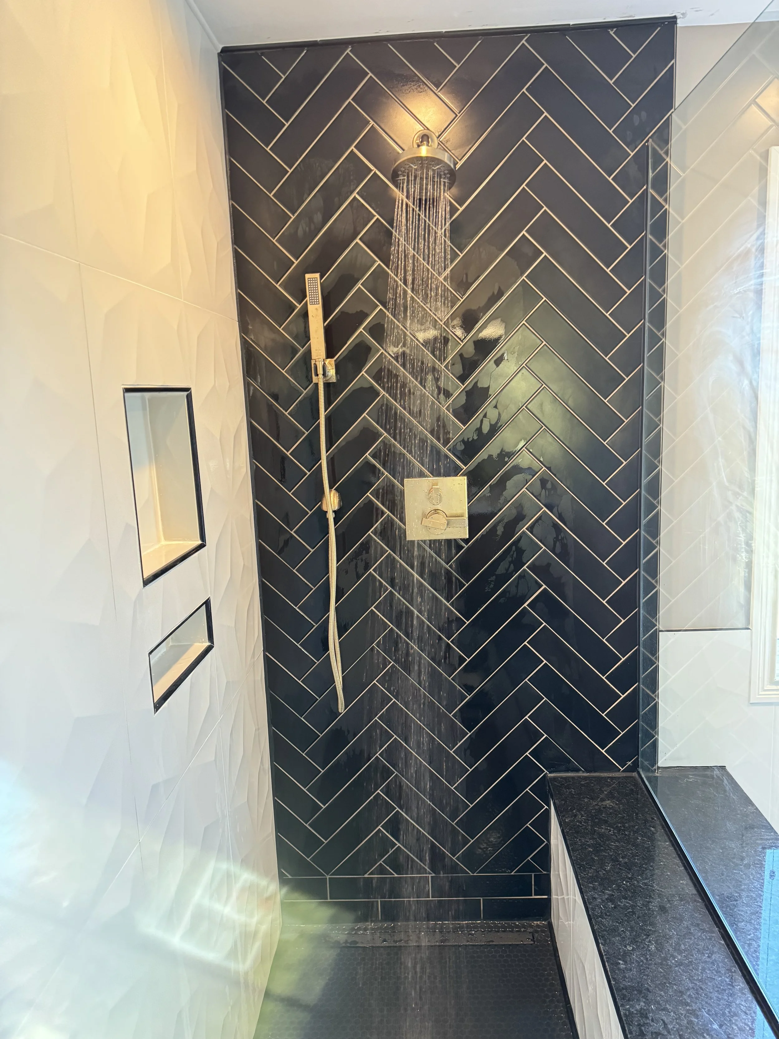 Shower area with black herringbone tiles, a rainfall showerhead, a handheld shower, and a built-in bench with a black granite surface.


Installed near Dayton Ohio