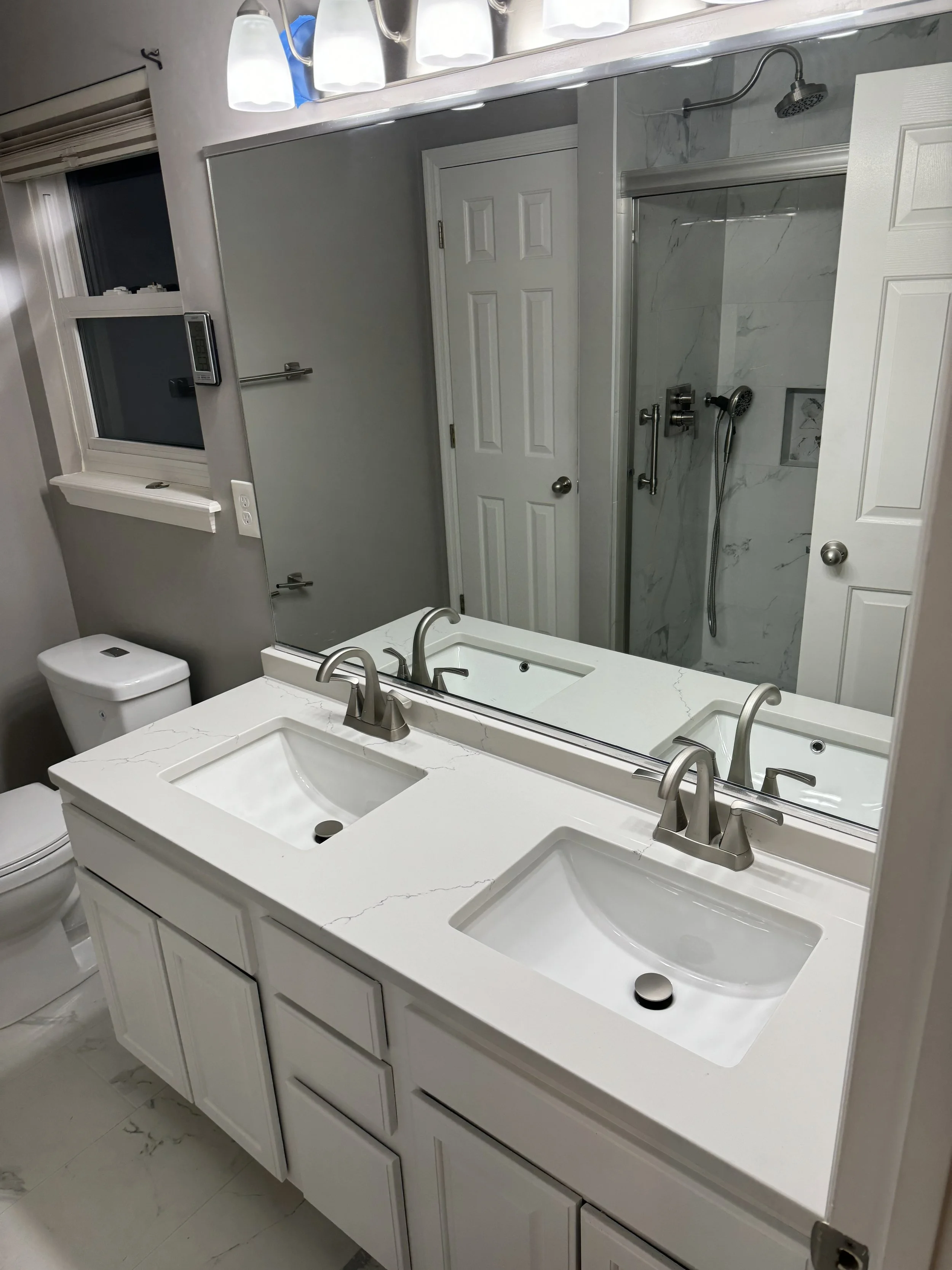 Bathroom with a white double vanity, large mirror, marble countertop, two sinks with brushed nickel faucets, a toilet, a window, and a glass shower with a handheld showerhead.


Installed near Fairfield Ohio 