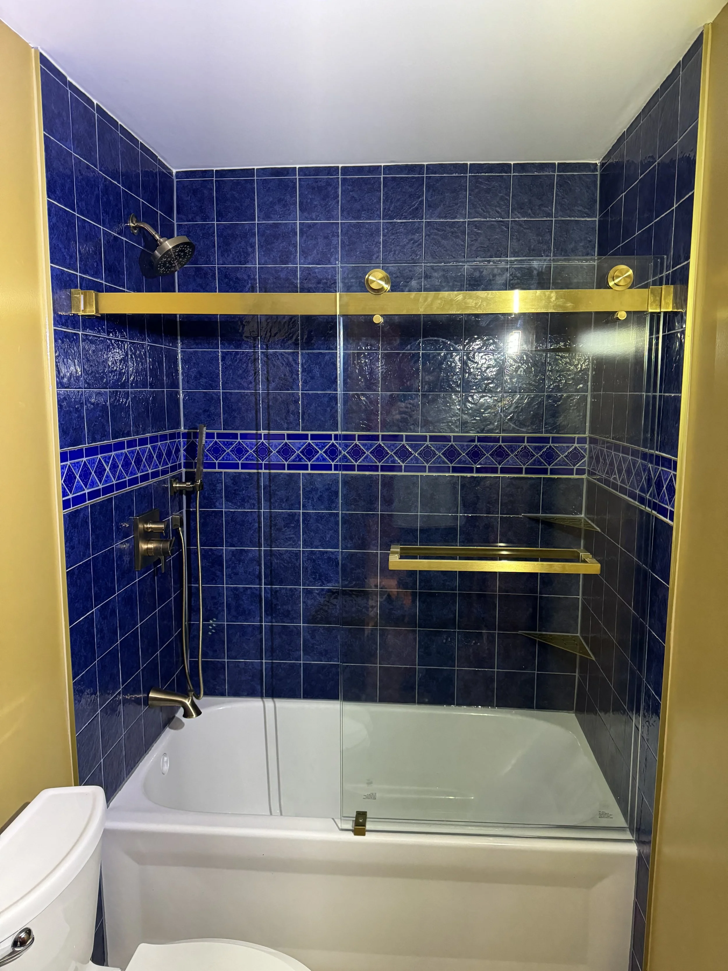 Bathroom with dark blue tiled shower area, brass shelves, glass shower door, showerhead, and a white bathtub. Part of a white toilet is visible in the foreground.



Installed near west Alexandria Ohio 