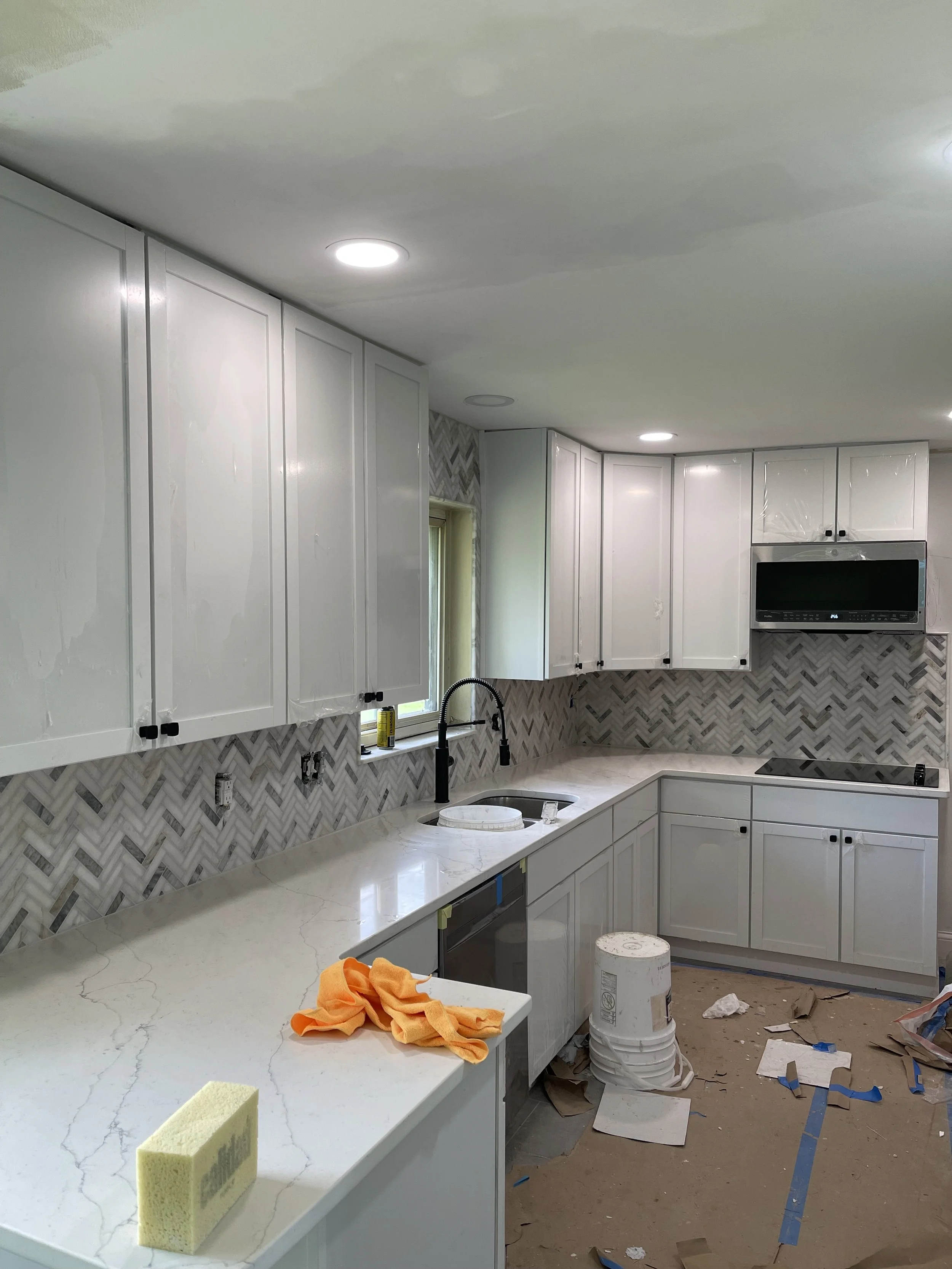 Kitchen under construction with white cabinets, marble countertop, herringbone tile backsplash, black faucet, and some construction tools and materials on the floor.

Installed near Ross Ohio
