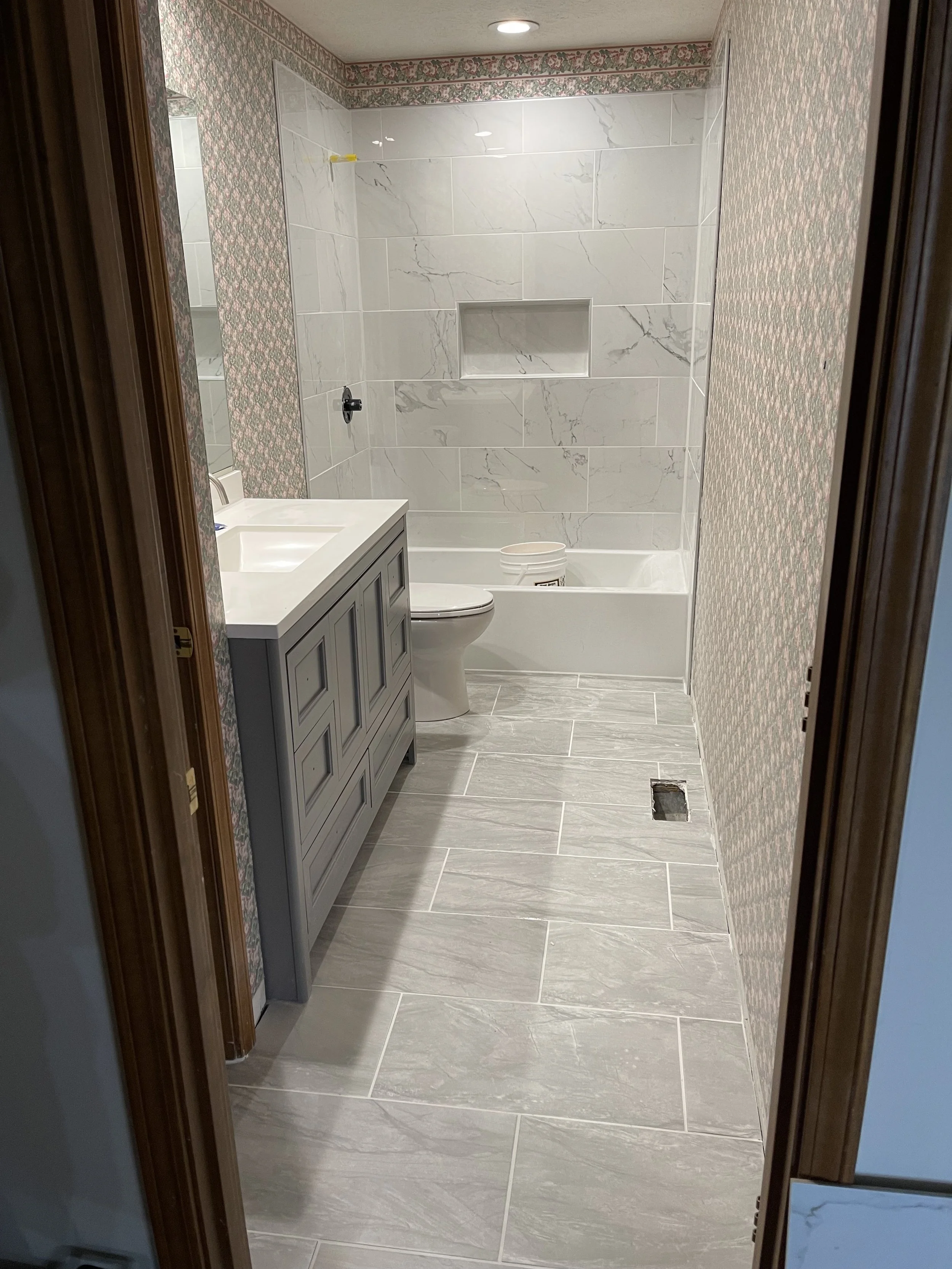Modern bathroom with light-colored marble tiles on the floor and wall, vanity with a sink, toilet, and bathtub with a built-in niche in the wall, and wallpaper with a floral pattern on the remaining walls.

Installed near Springboro Ohio