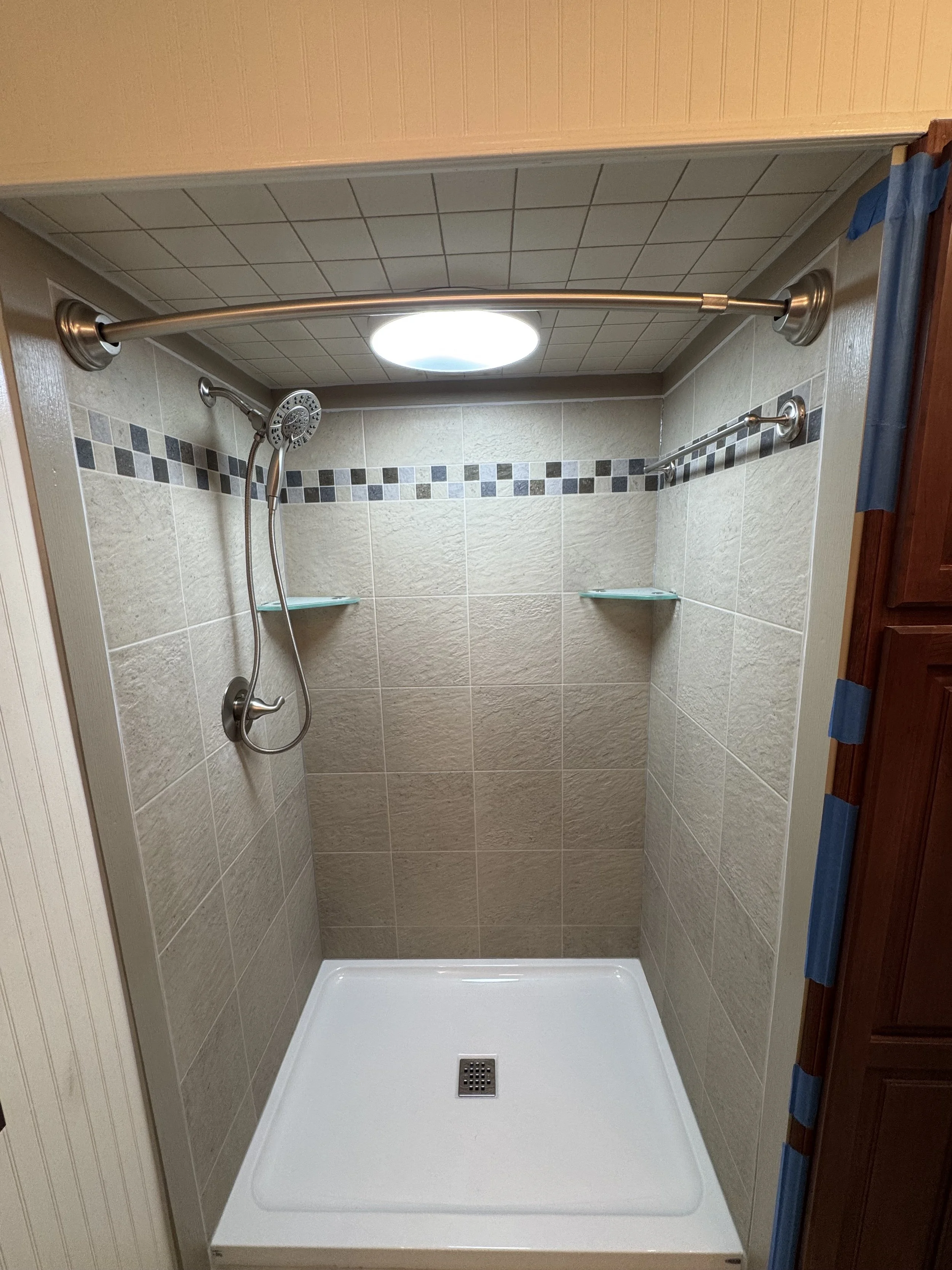 Empty shower with beige tile walls, a small square shower pan, a handheld showerhead, a curved shower curtain rod, and glass shelves.

Installed near Springboro ohio