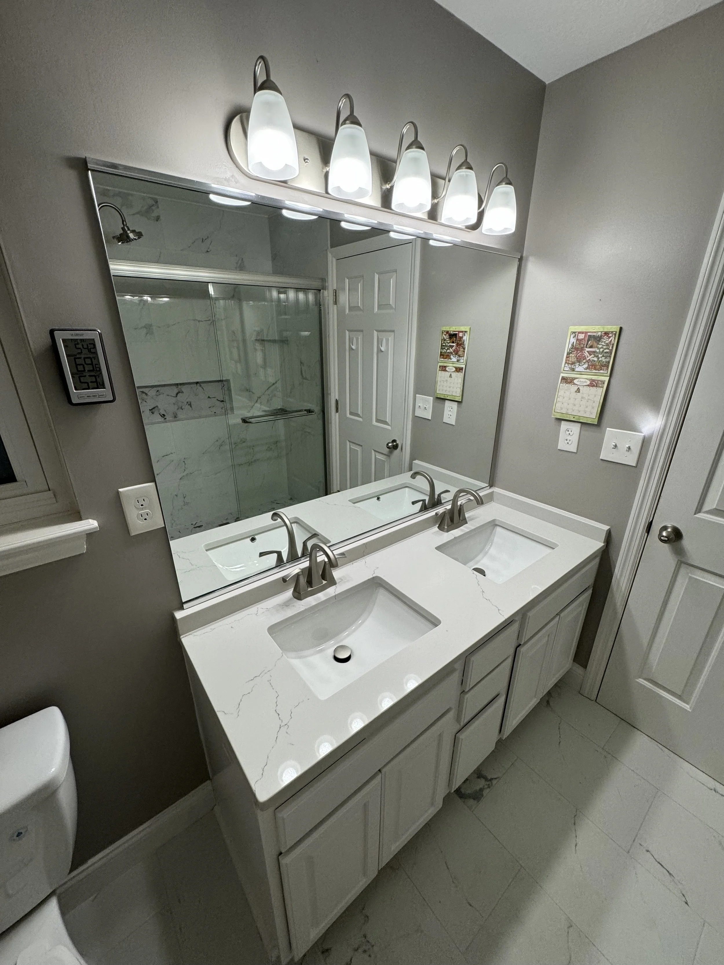 Bathroom with white marble double sink vanity, large mirror, four light fixtures, shower with glass door, wall switches and calendar on wall



Installed in Fairfield Ohio 