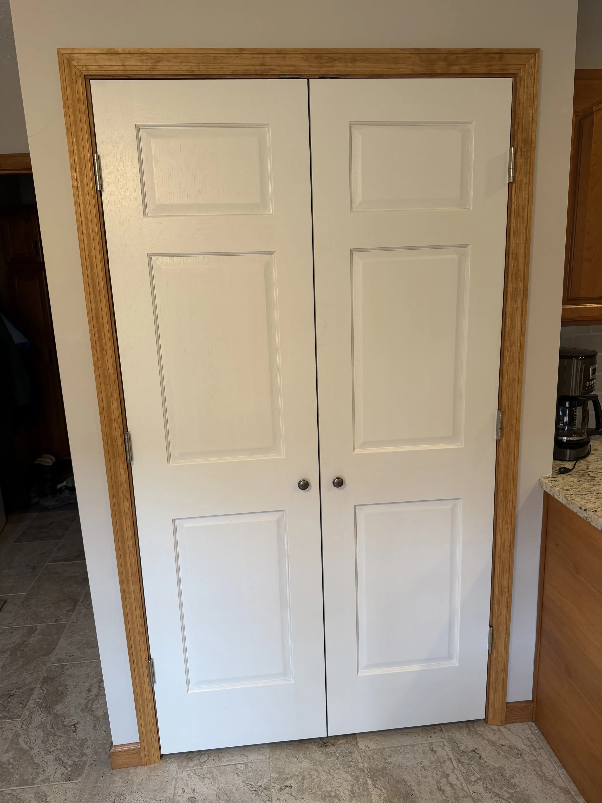 White double closet doors with wooden frame in a kitchen.