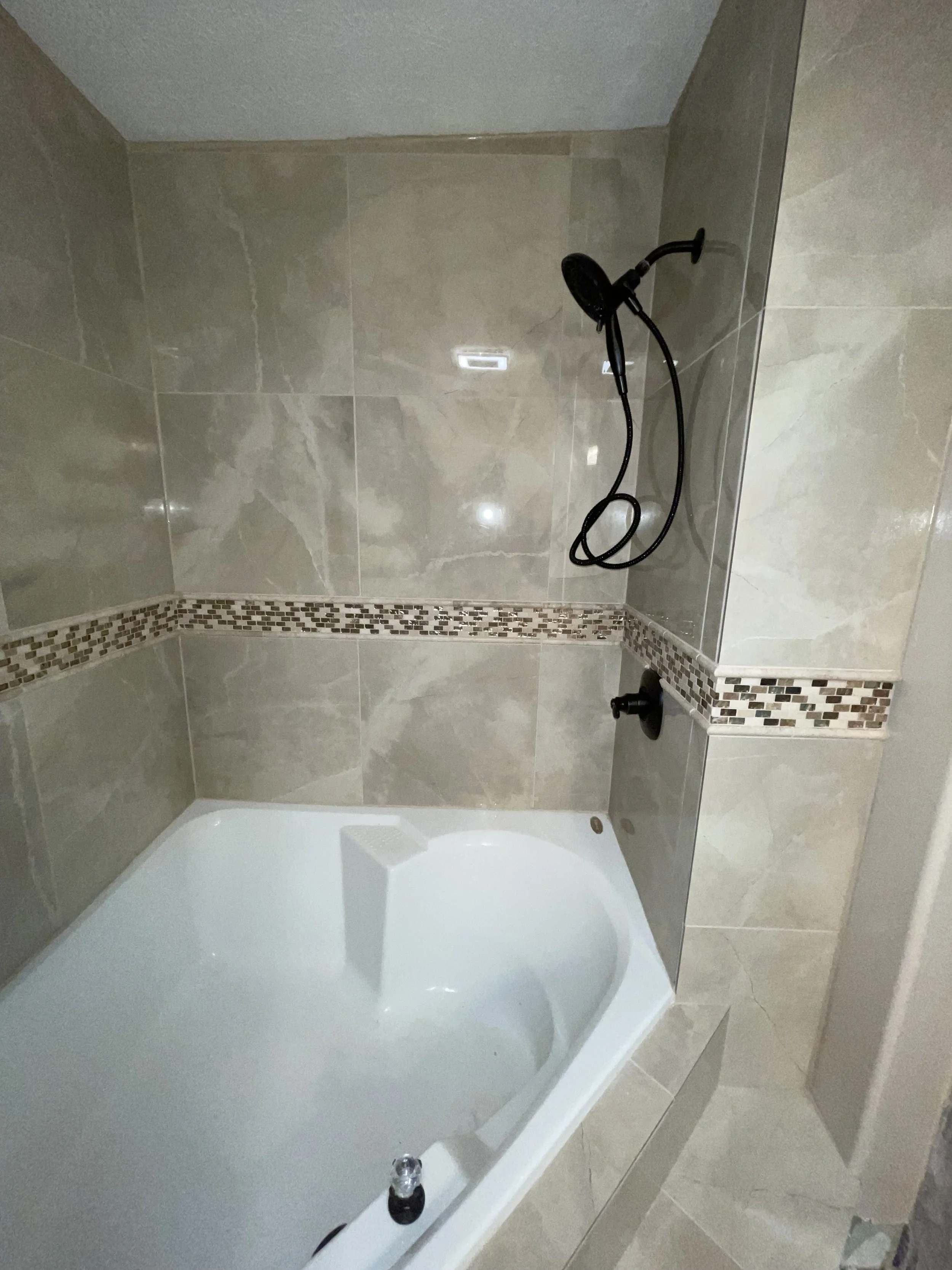 Bathroom shower with a built-in bathtub, tiled walls, and a black showerhead with a flexible hose.