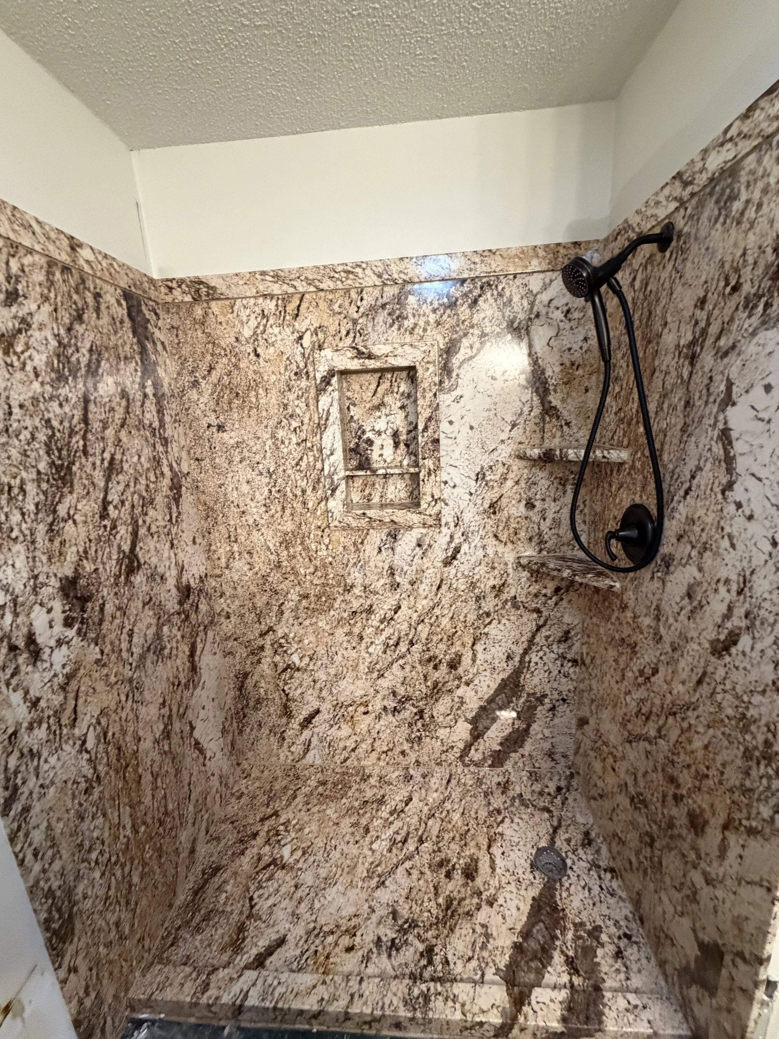 A shower with brown and beige marble walls and floor, a built-in niche, and a black handheld showerhead.

Installed near west Alexandria Ohio 