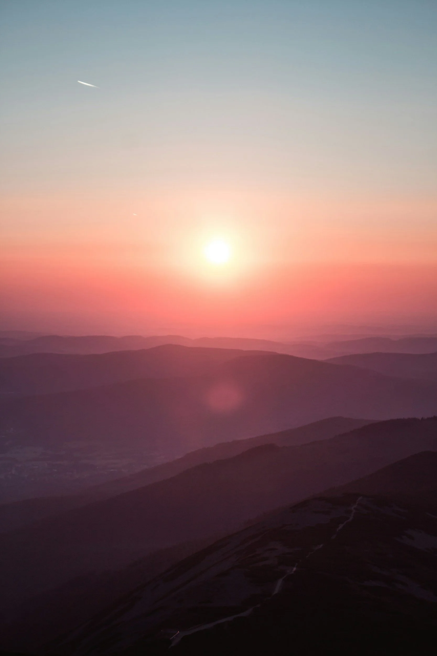 Sunset over mountains with pink and orange sky and two airplanes in the distance.