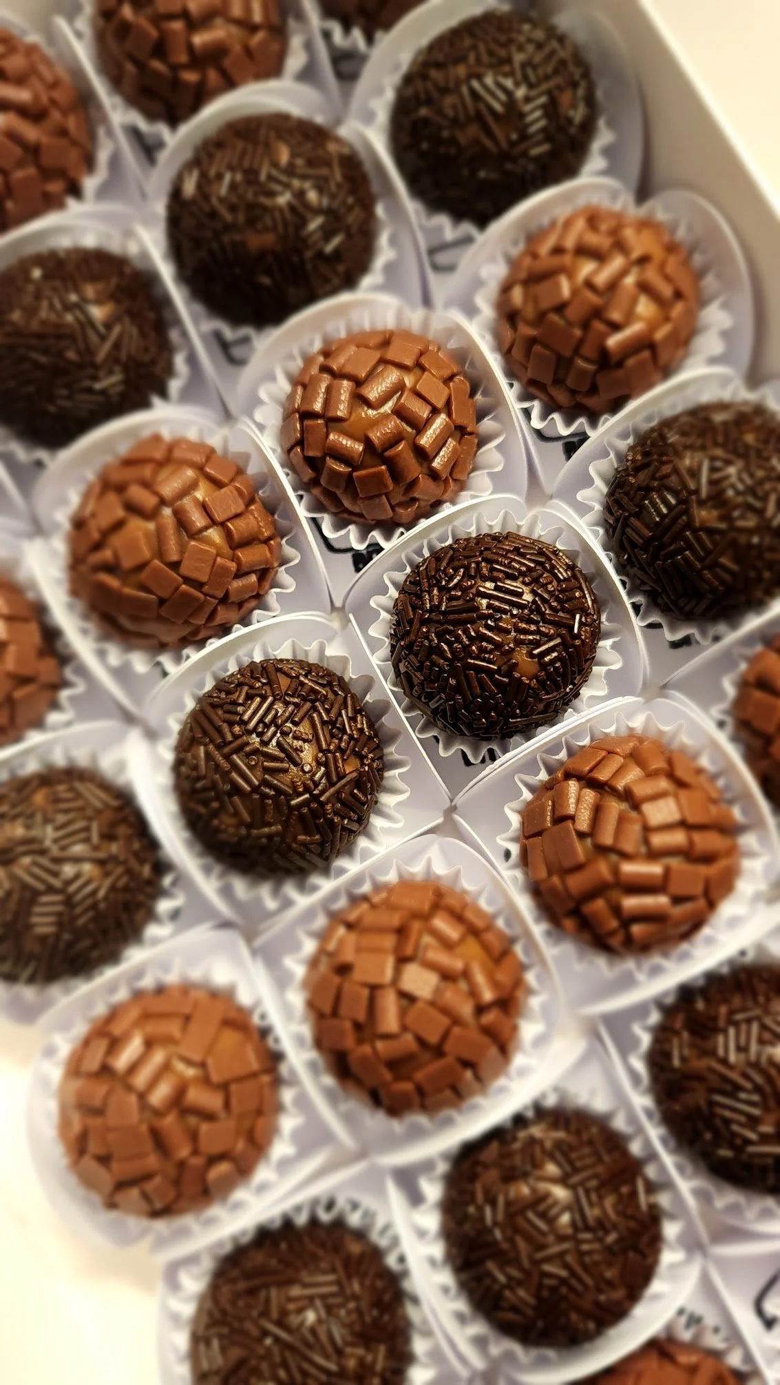 Close-up of handcrafted Brazilian brigadeiros with assorted finishes, presented in individual paper cups.