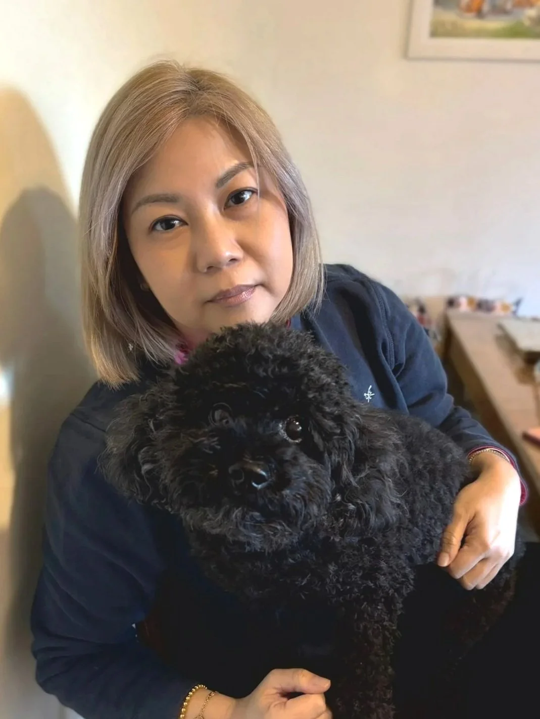 Woman with shoulder-length blonde hair holding a black poodle dog inside a home.