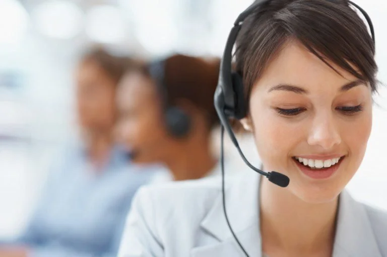 A smiling woman wearing a headset, working in a call center environment.