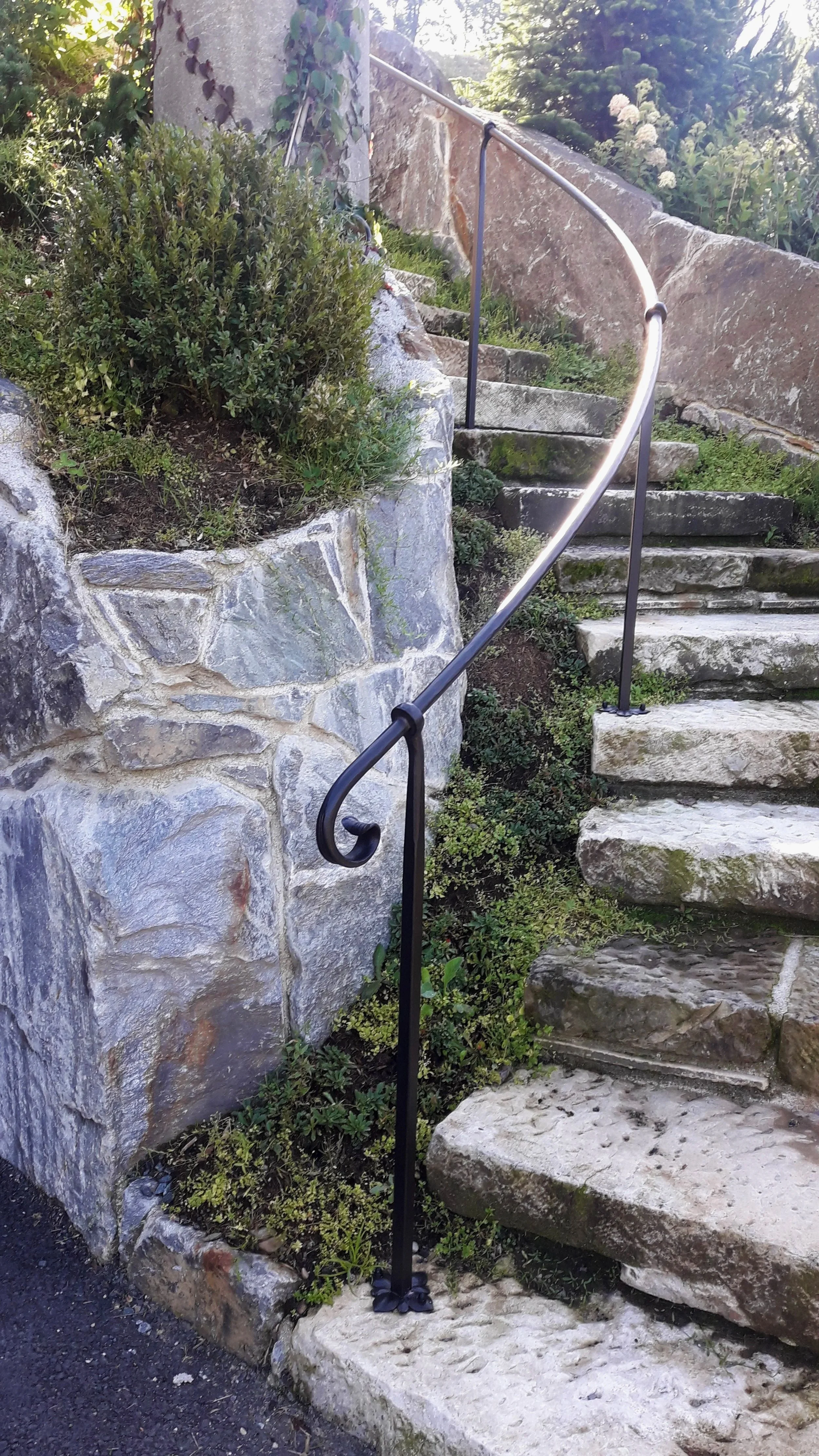 Steinerne Treppe mit schwarzem Geländer neben einem Steingarten mit Büsche und Pflanzen auf einer Neugestaltung im Freien.