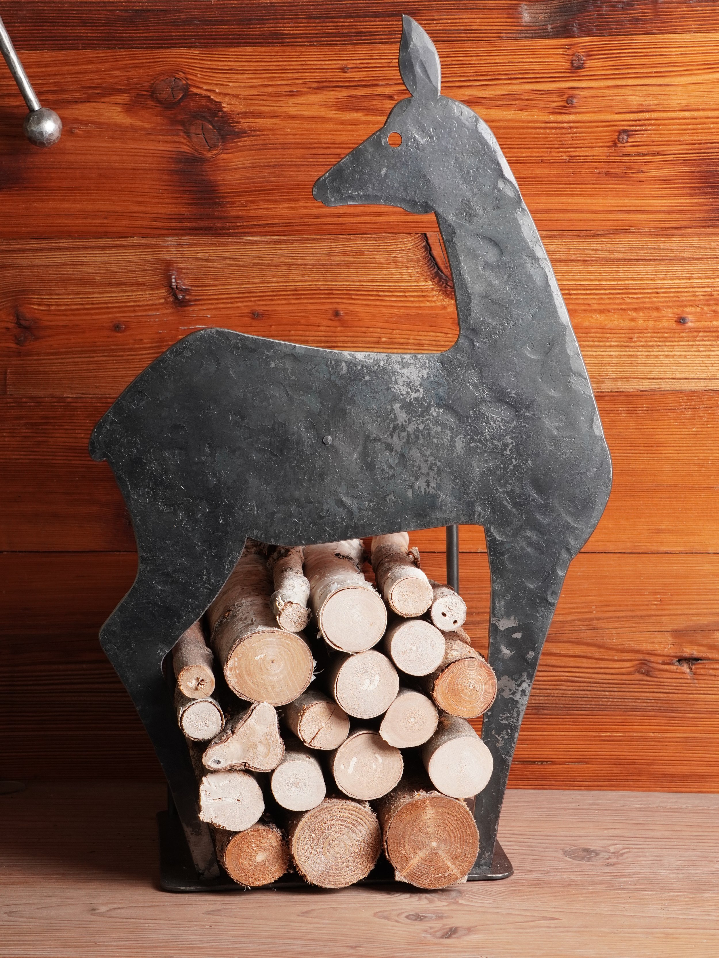 Stapel Holzscheite in einem Metall-Feuerschale in Form eines Esels vor einer Holzvertäfelung.