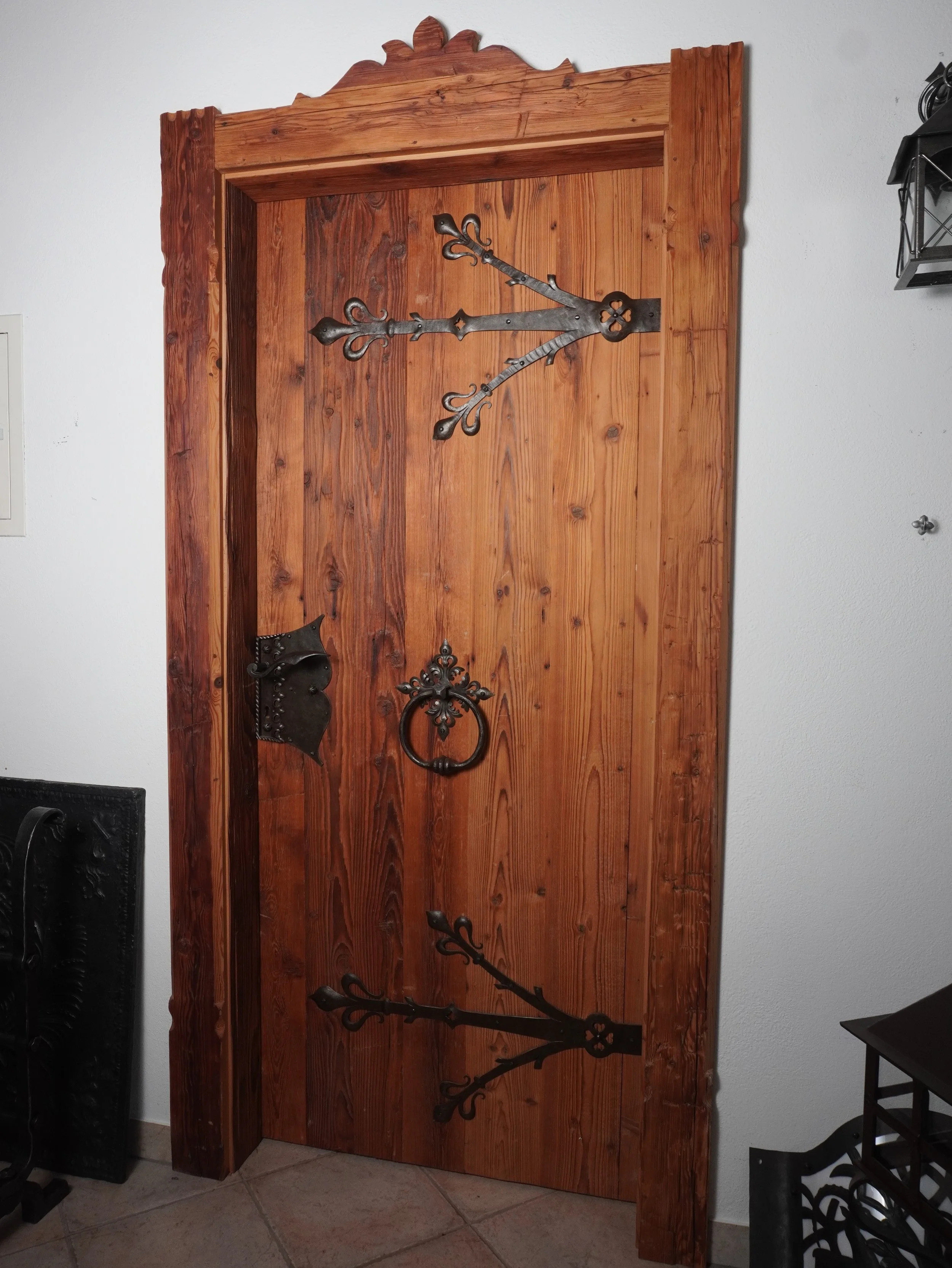 Eine Tür aus Holz mit einer verzierenden Umrahmung und verzierte schwarze Eisenbeschläge inklusive eines Türknaufs, eines Beschlags und eines großen Dekorstücks.