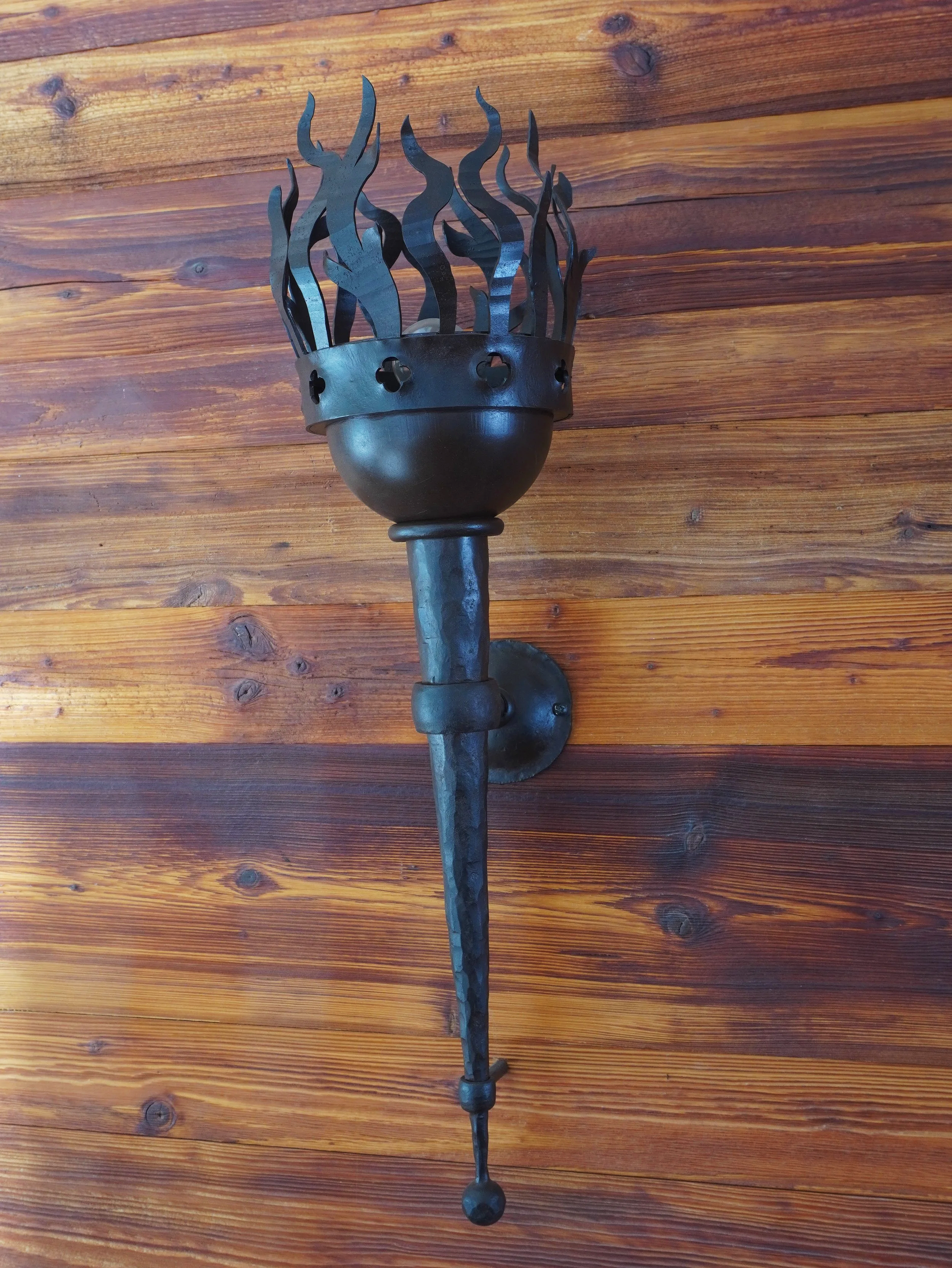 Schwarzes Eisen-Torch in Form eines Flammen-Vorbilds, an einer Holz-Wand montiert.