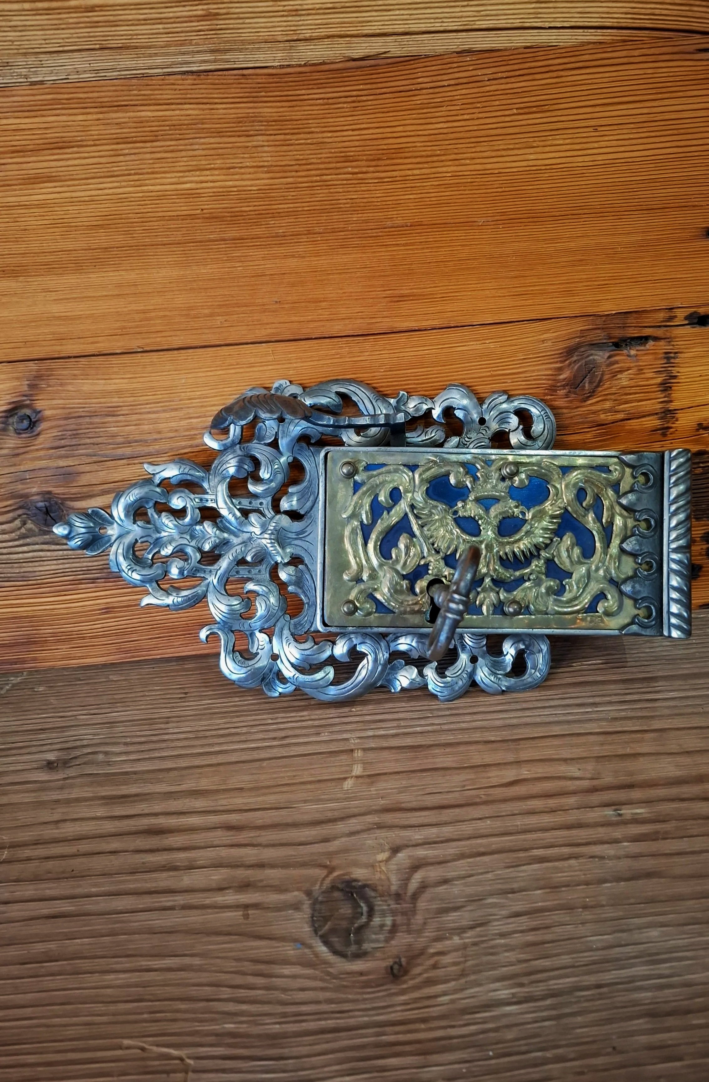 Antiker, kunstvoll verzierter Türklopfer mit Delfinen und einem Adler auf einem Holzfußboden.
