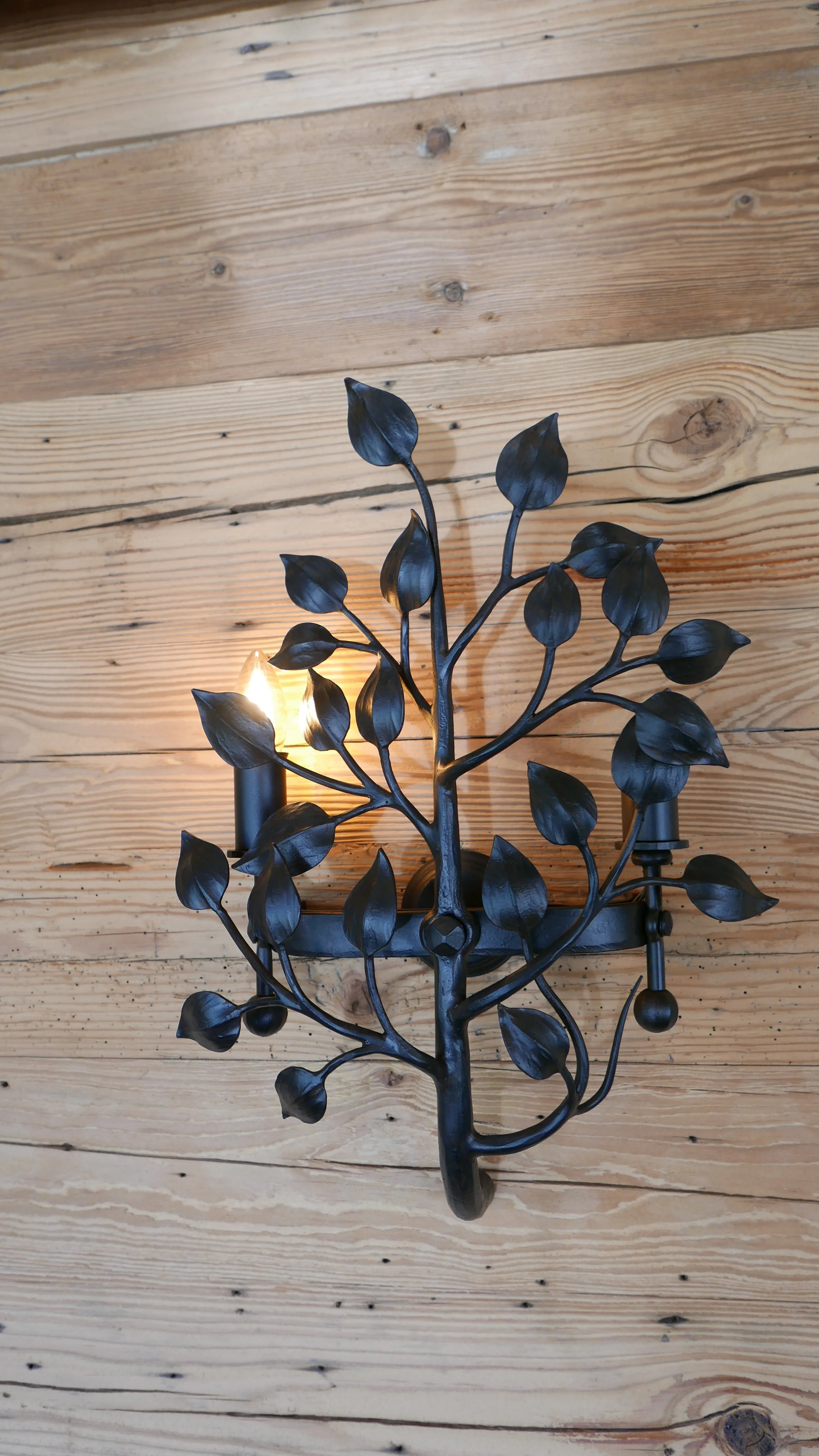 Wandlampe in Form eines Baum mit schwarzen Blättern vor einer Holzvertäfelung