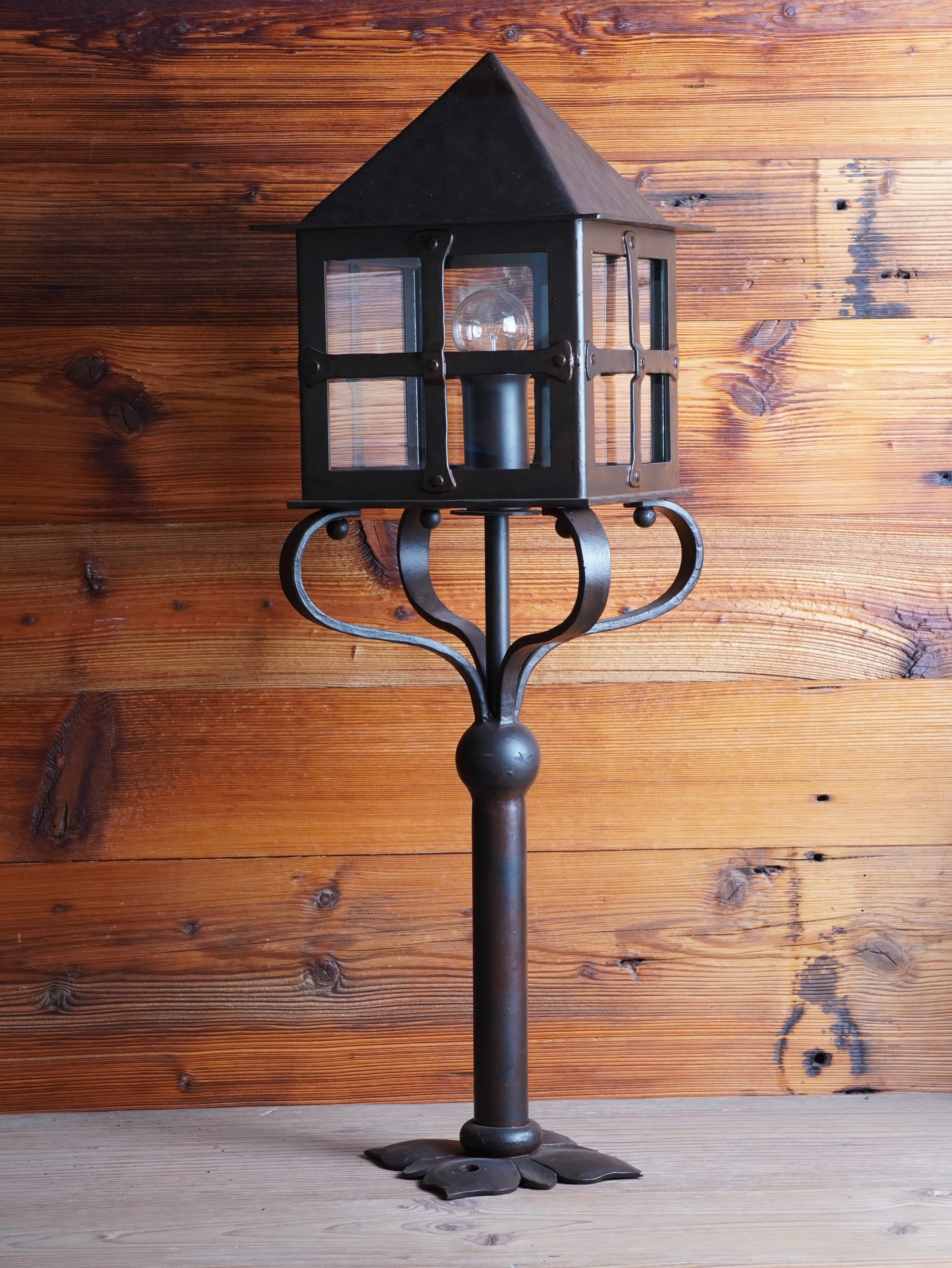 Eine hausartige Laterne auf einem Metallpfosten vor Holzvertäfelung.
