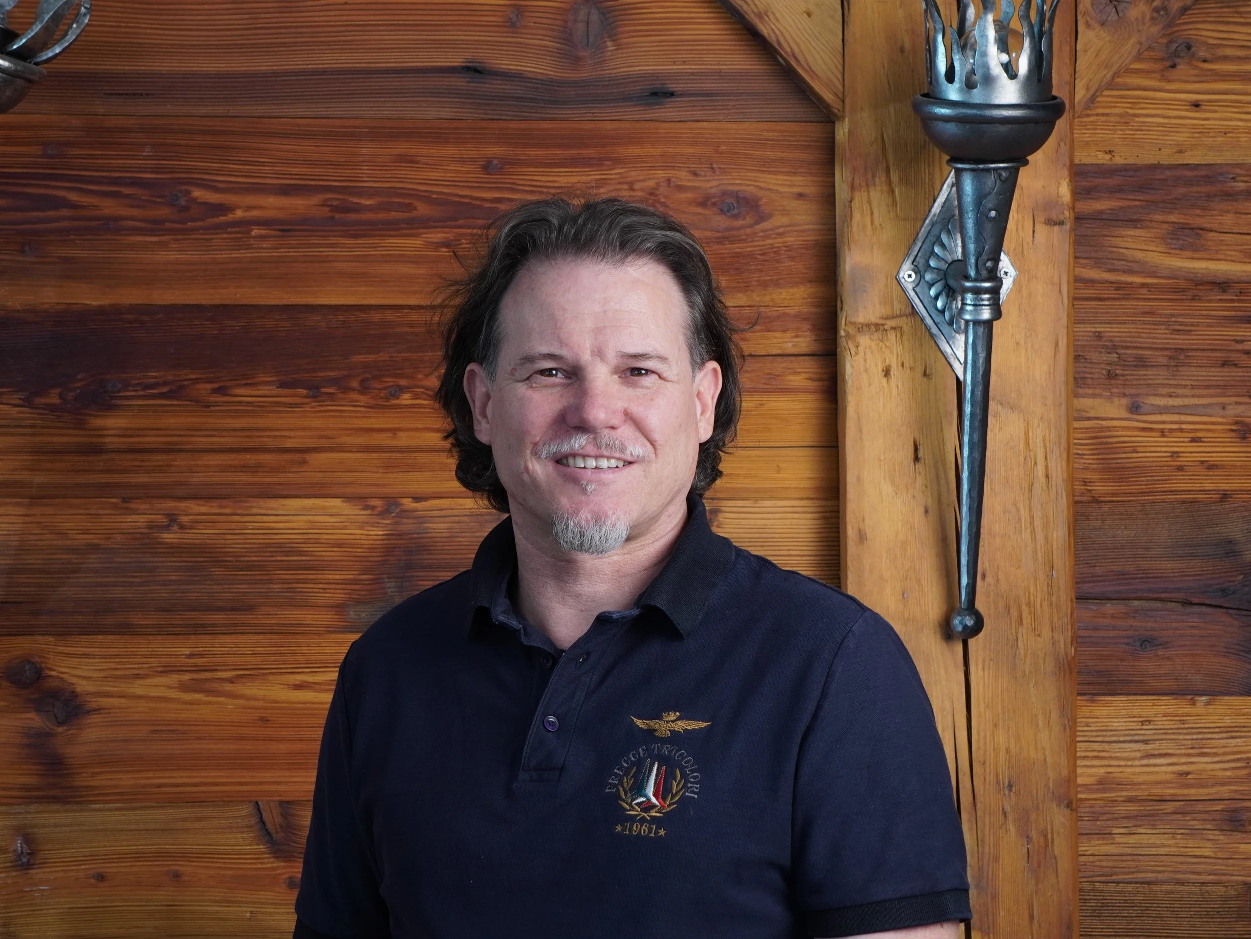 Ein Mann steht vor einer holzvertäfelten Wand mit einer dekorativen Wandlampe auf der rechten Seite.