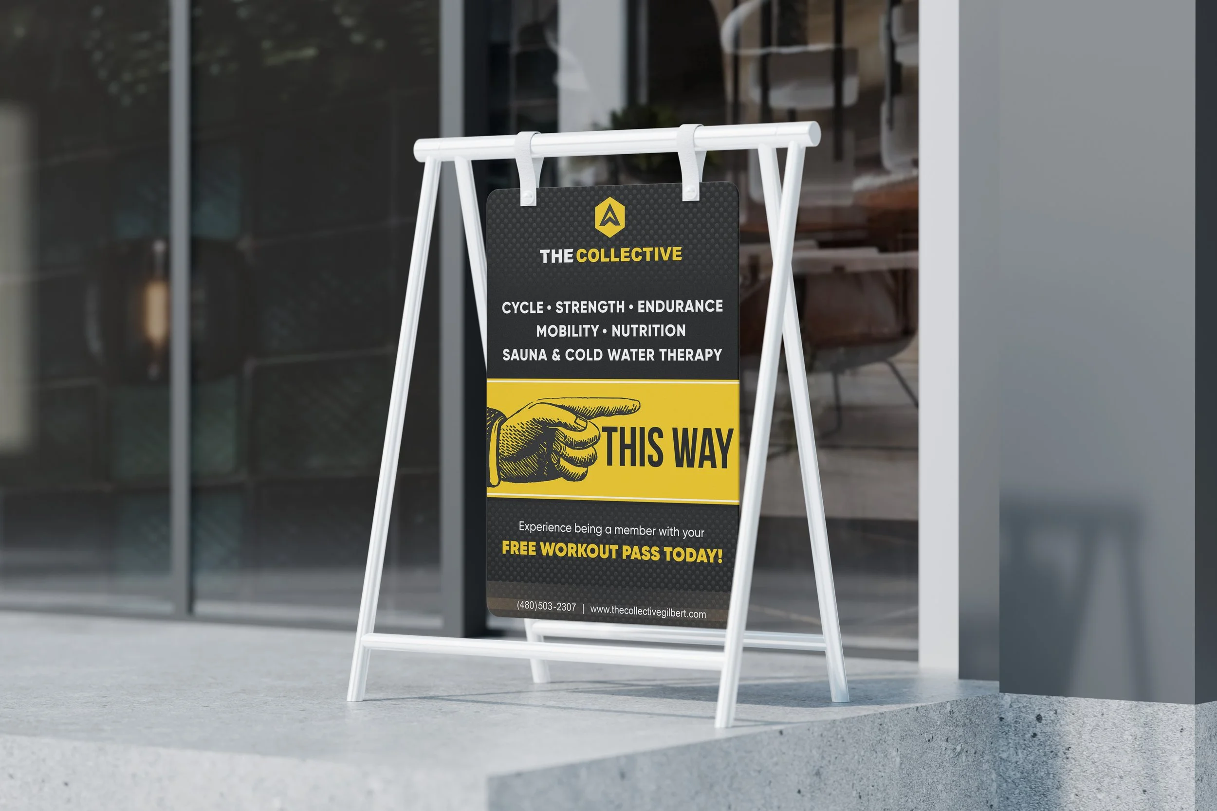 A black and yellow sign positioned outside a gym advertises membership benefits and a free workout pass, with a hand pointing to the right.