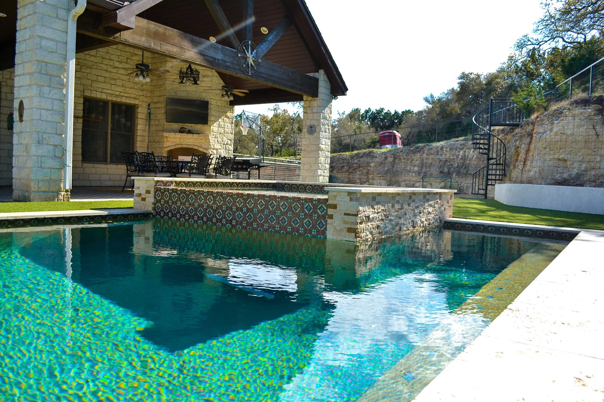 Backyard with a swimming pool, outdoor seating area, stone house wall, and spiral staircase leading to the hillside.
