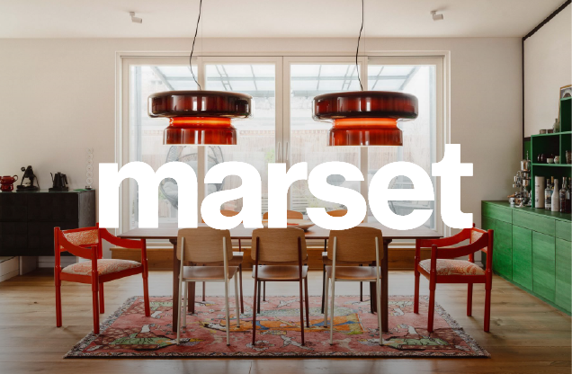 Modern dining room with seven chairs (two red, five wood) around a wooden table, large windows behind, vintage patterned rug, two large copper pendant lights, and green cabinets with barware on the right.