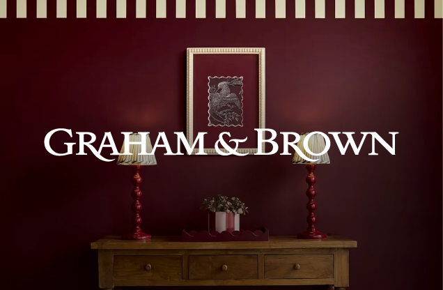 Interior decor with a wooden sideboard, two red lamps, a framed artwork, and Graham & Brown logo on a maroon wall