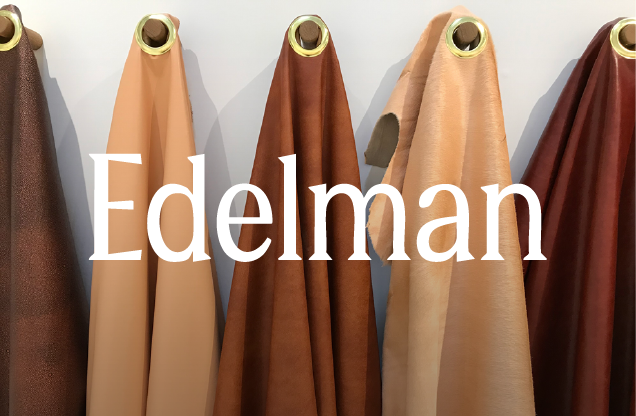 Several rolls of leather or fabric material in different shades, displayed on a wall with gold hooks, with the word 'Edelman' written across them.