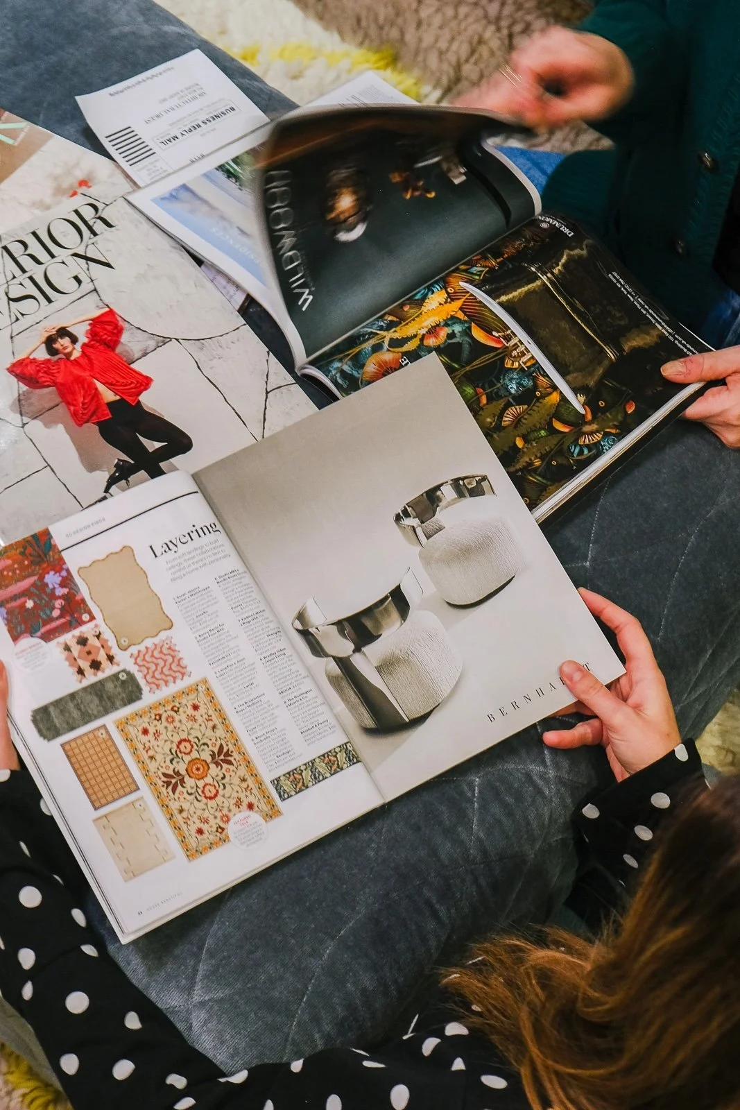 People sitting on a couch, flipping through various interior design magazines with furniture, fashion, and decor images.