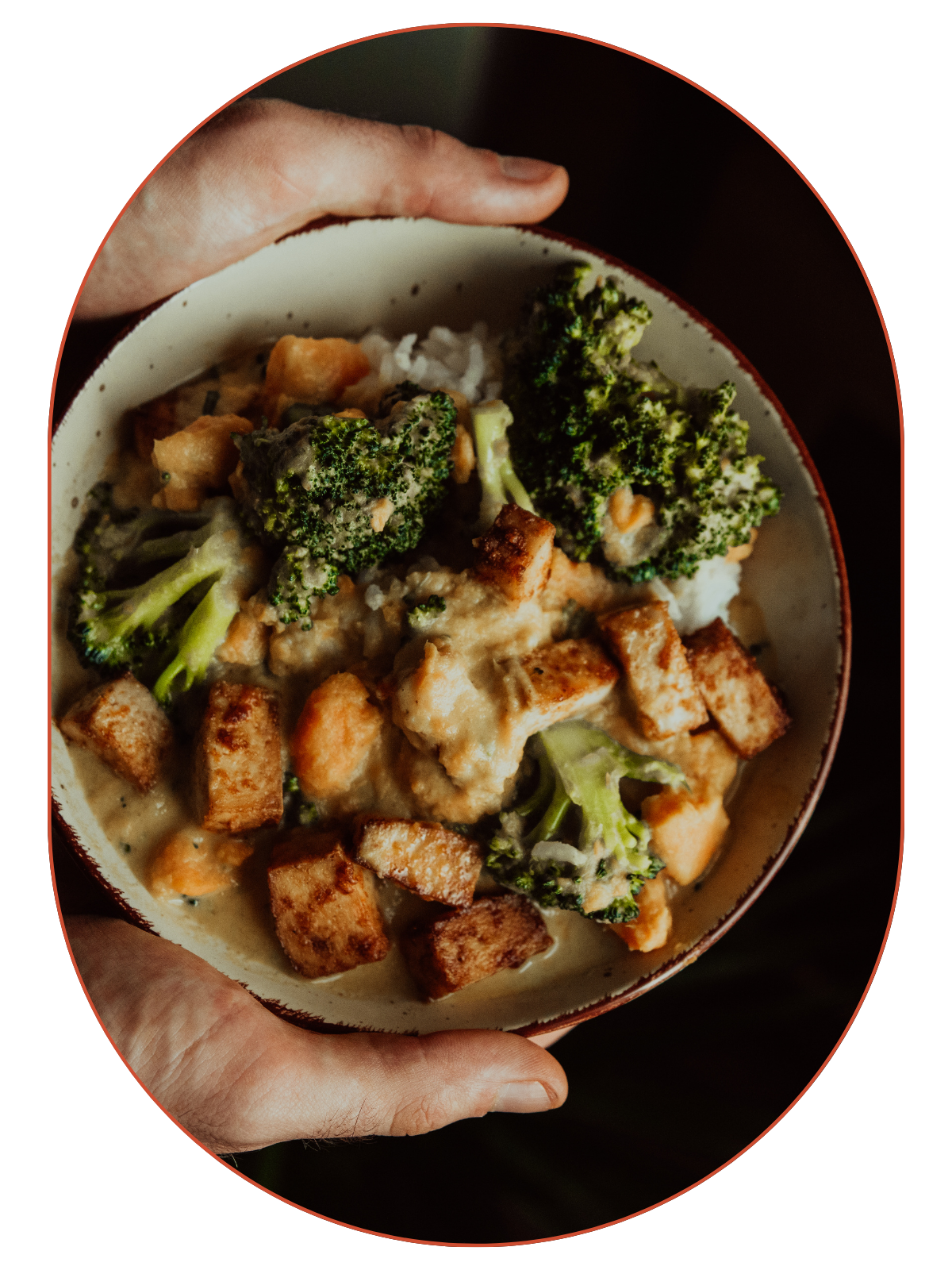 A bowl of creamy chicken and broccoli casserole topped with toasted bread cubes, held by a person's hand.