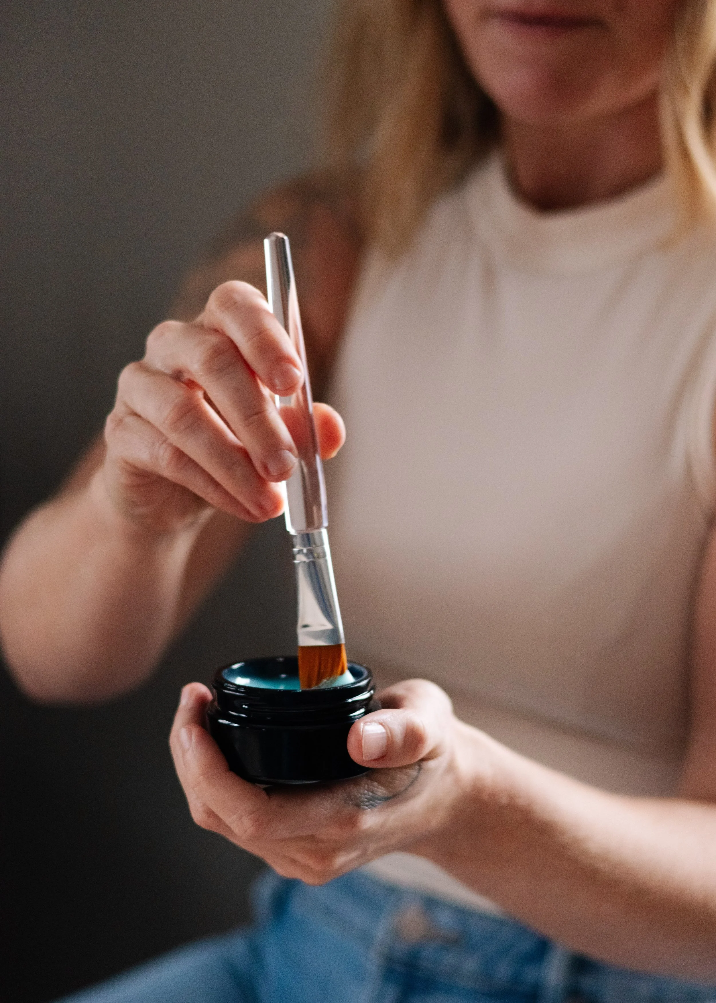 A woman holding a black container and using a glass dropper to fill it with a brown liquid.